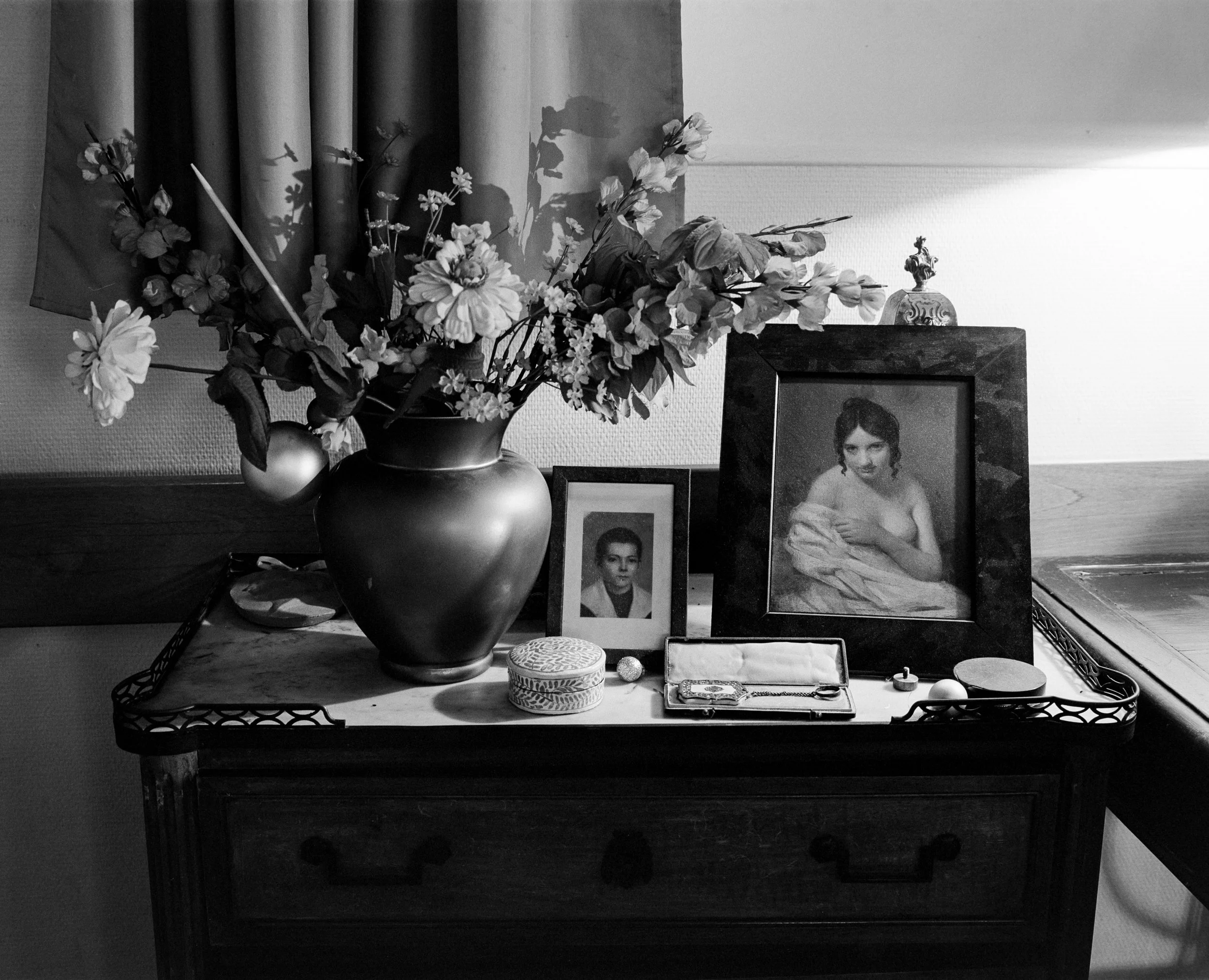 Une composition de photos anciennes, un vase avec des fleurs, une boîte et divers petits objets posés sur un meuble en bois