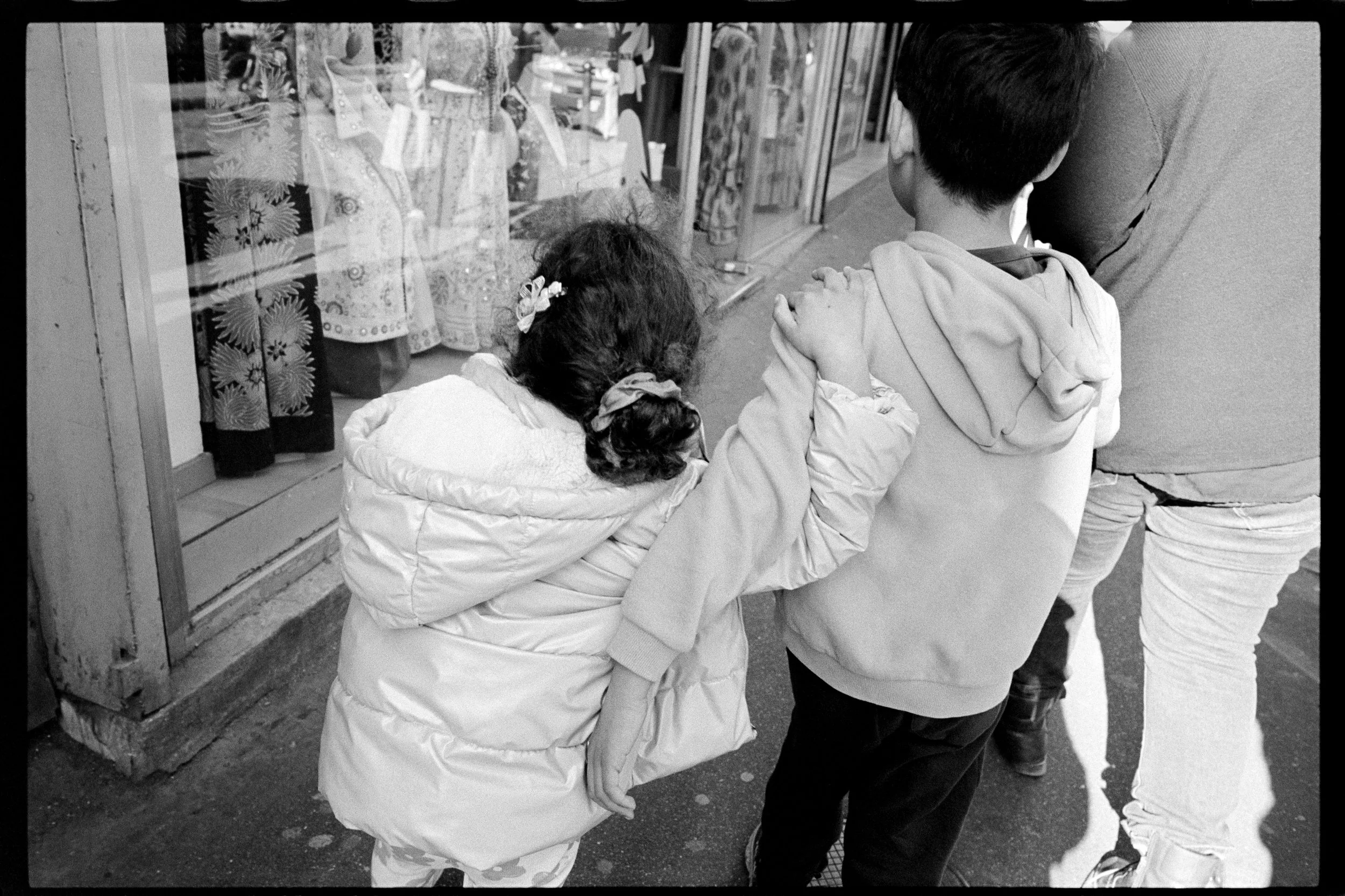Trois enfants qui attendent en file, deux regardant un magasin de vêtements.