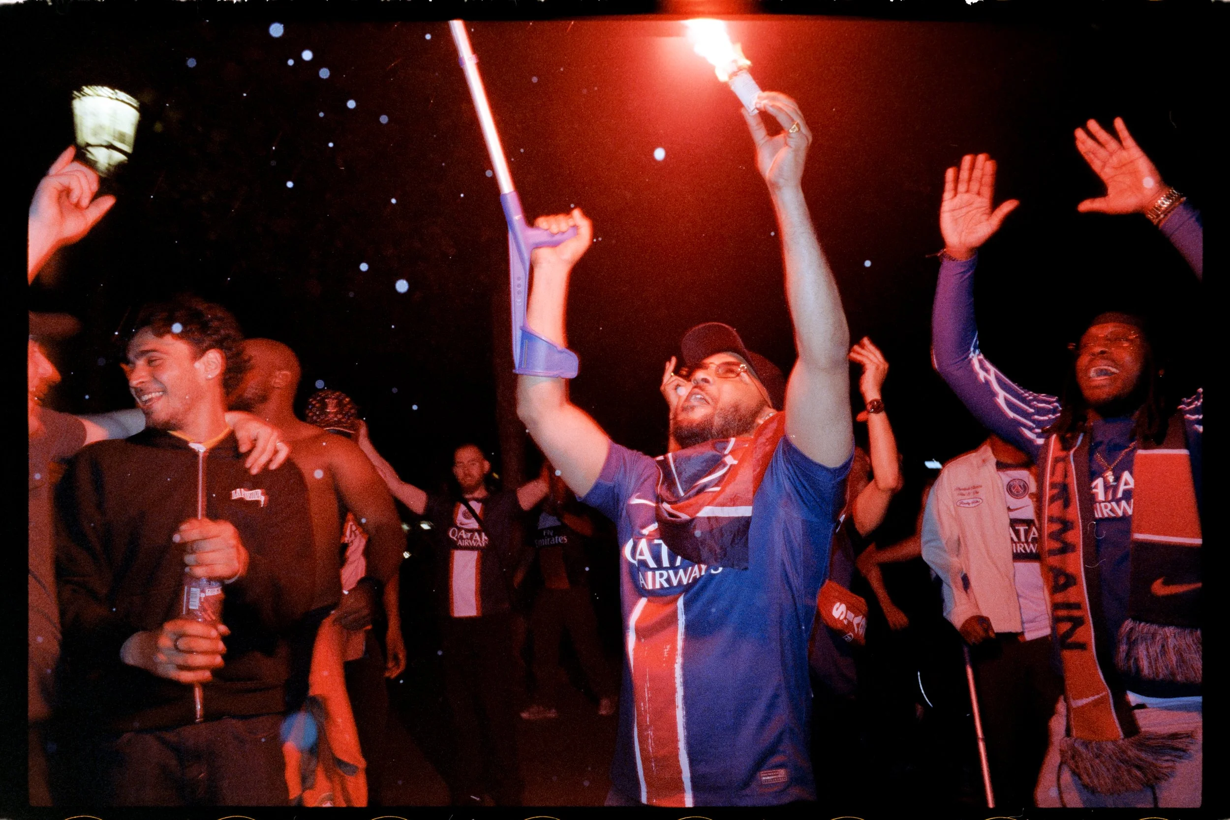Groupe de personnes en célébration, certains portant des maillots de football, dans une fête nocturne avec des lumières rouges et des confettis.