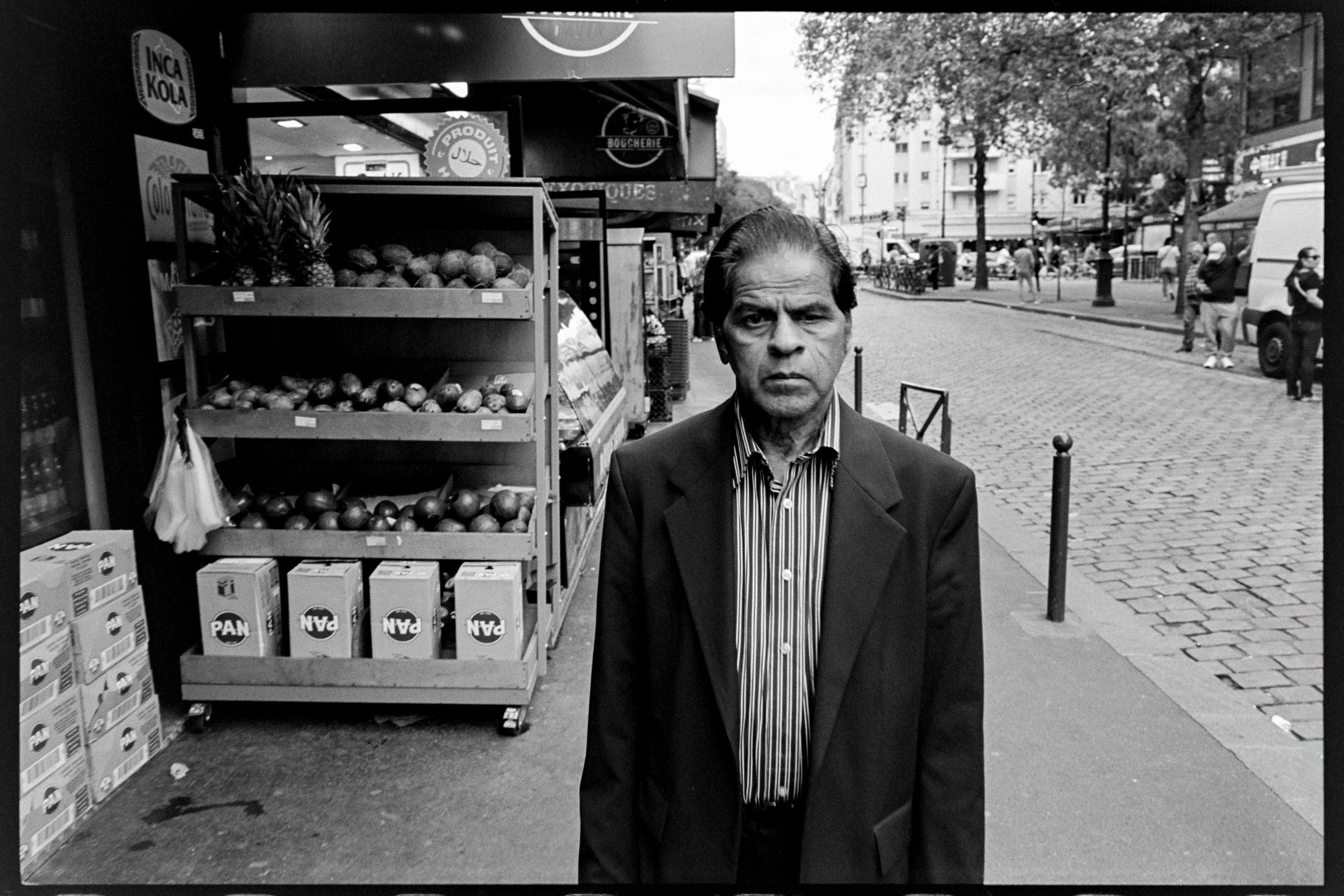Homme d'affaires en costume sur un trottoir, contexte urbain avec stands de fruits et autres passants