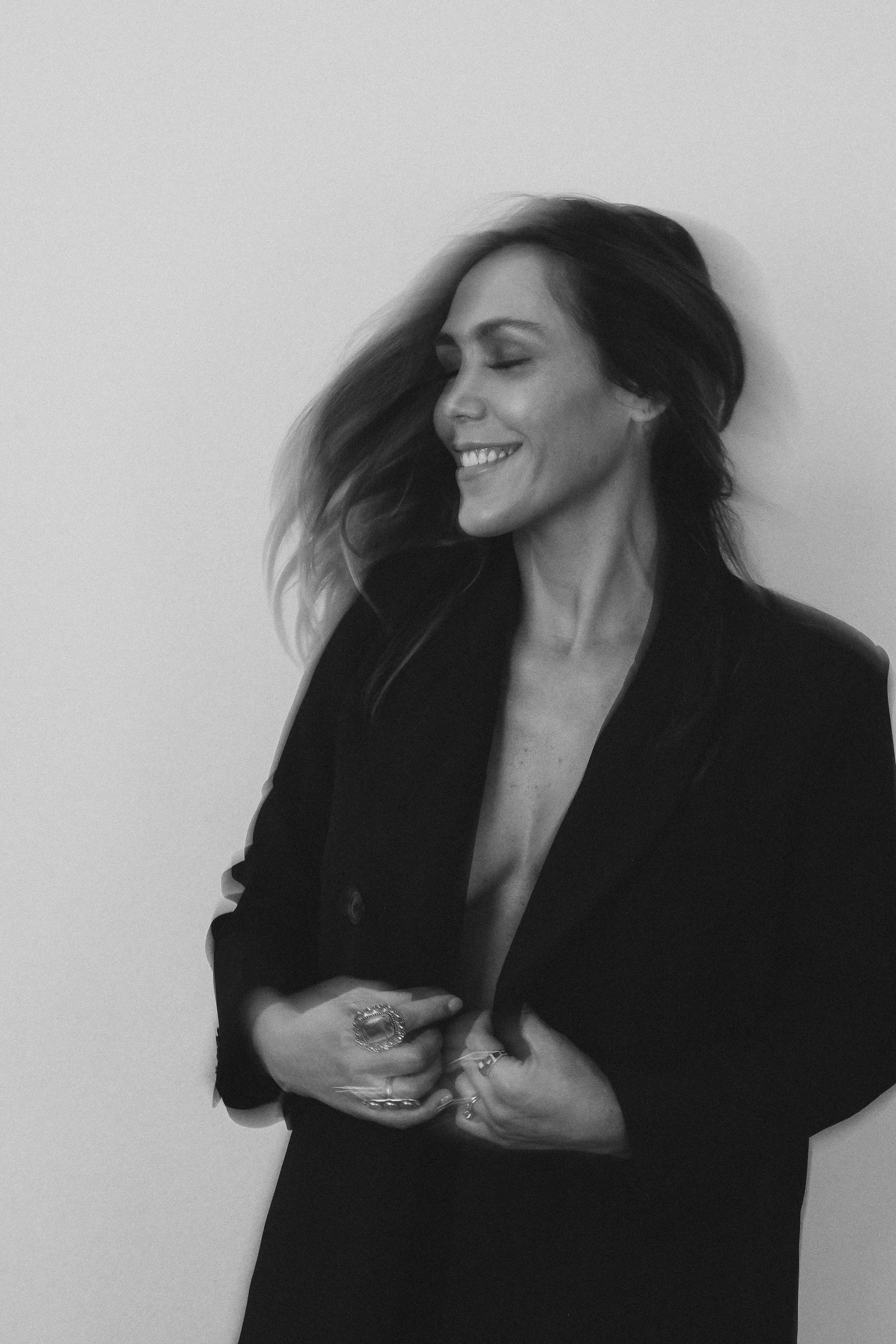 Kristin Thompson laughing in a black blazer, black and white portrait.