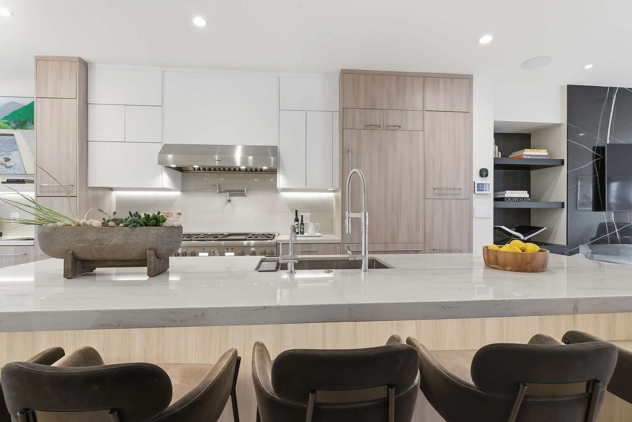 Modern kitchen with beige cabinetry, white countertops, stainless steel appliances, and a kitchen island with three chairs.
