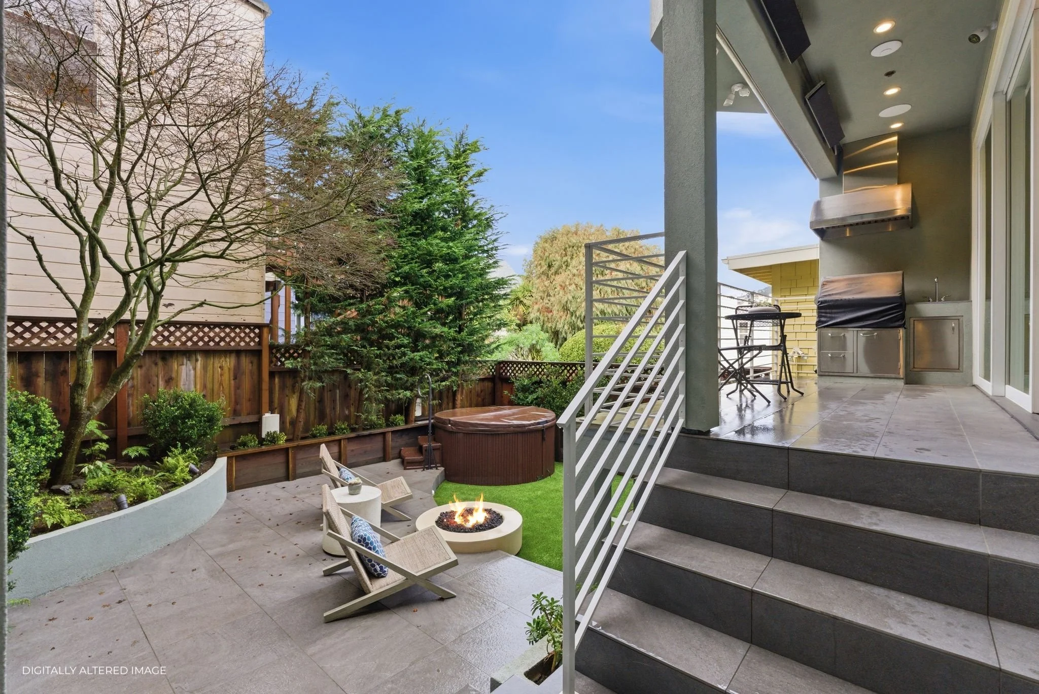 An outdoor patio with chairs and a fire pit, adjacent to a balcony with a grill and bar table, surrounded by trees and a wooden fence.