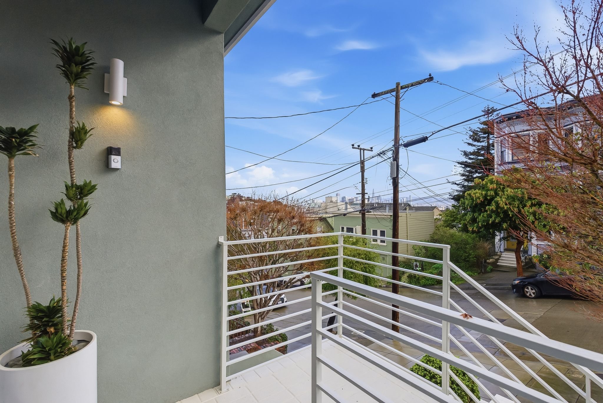View from a balcony showing power lines, trees, and houses in a neighborhood under a blue sky.