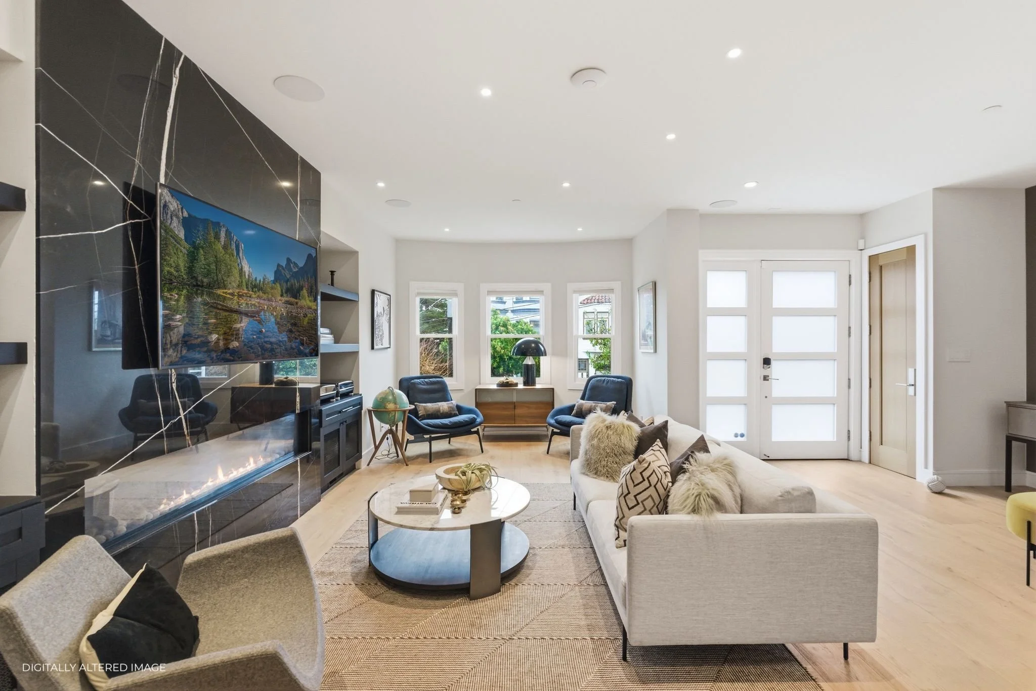 Modern living room with a white sofa, beige armchair, black chairs, fireplace, wall-mounted TV, and large windows letting in natural light.