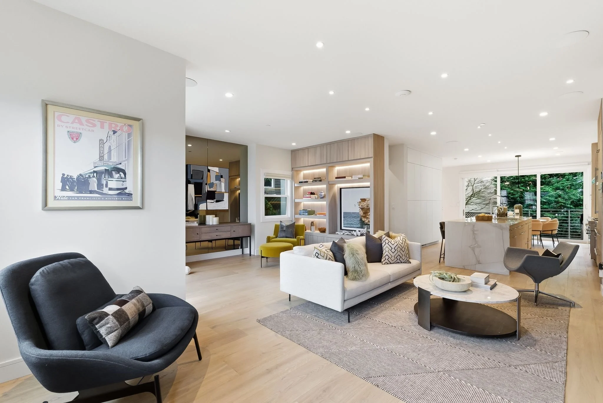 Open-concept living room and kitchen with modern decor, a white sofa with throw pillows, a marble-topped coffee table, a black chair with a pillow, and sliding glass doors leading to a balcony with greenery.