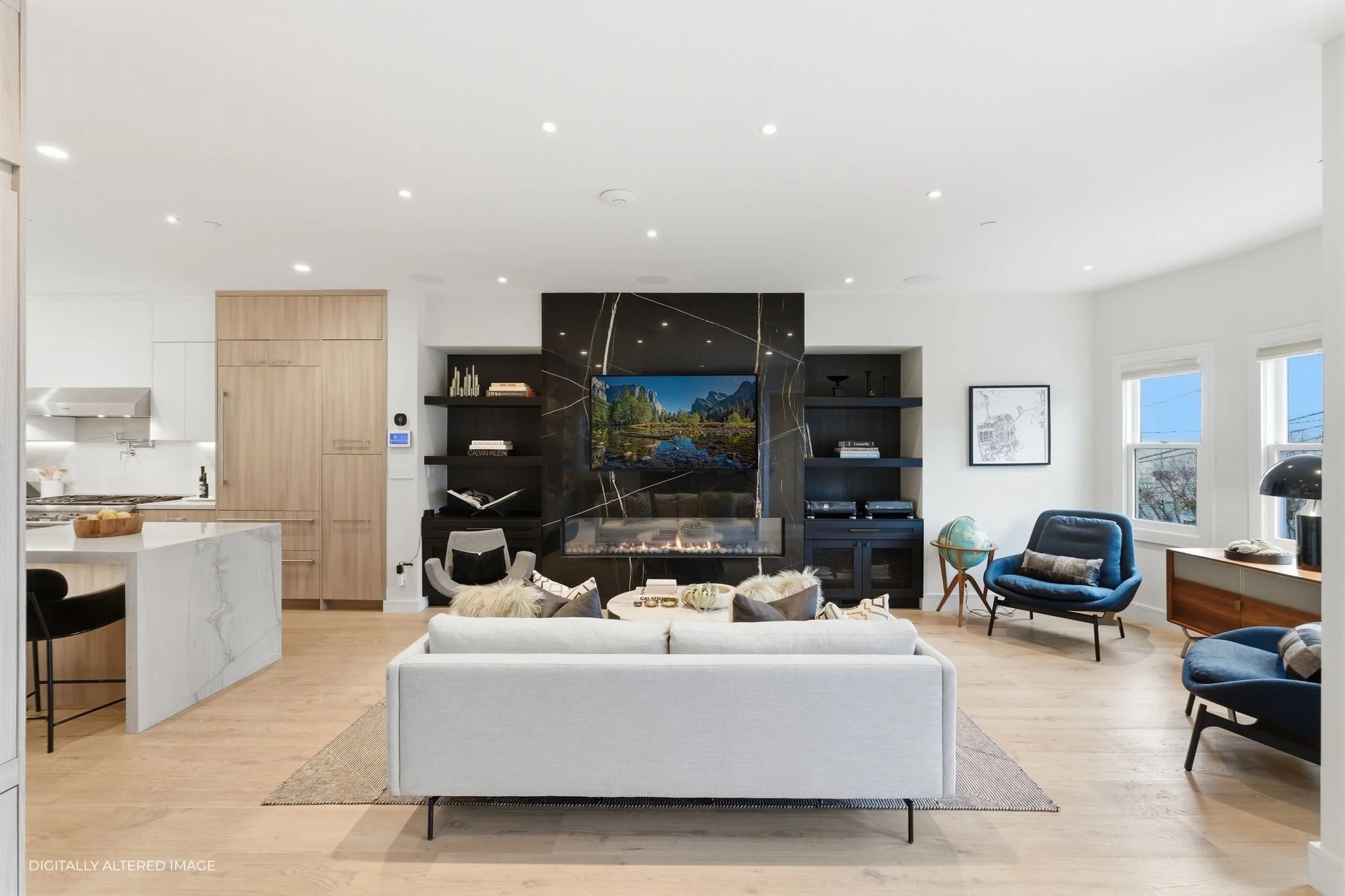 Modern living room with white sofa, black armchairs, wood flooring, built-in shelves, a black marble fireplace with a television, and multiple windows letting in natural light.
