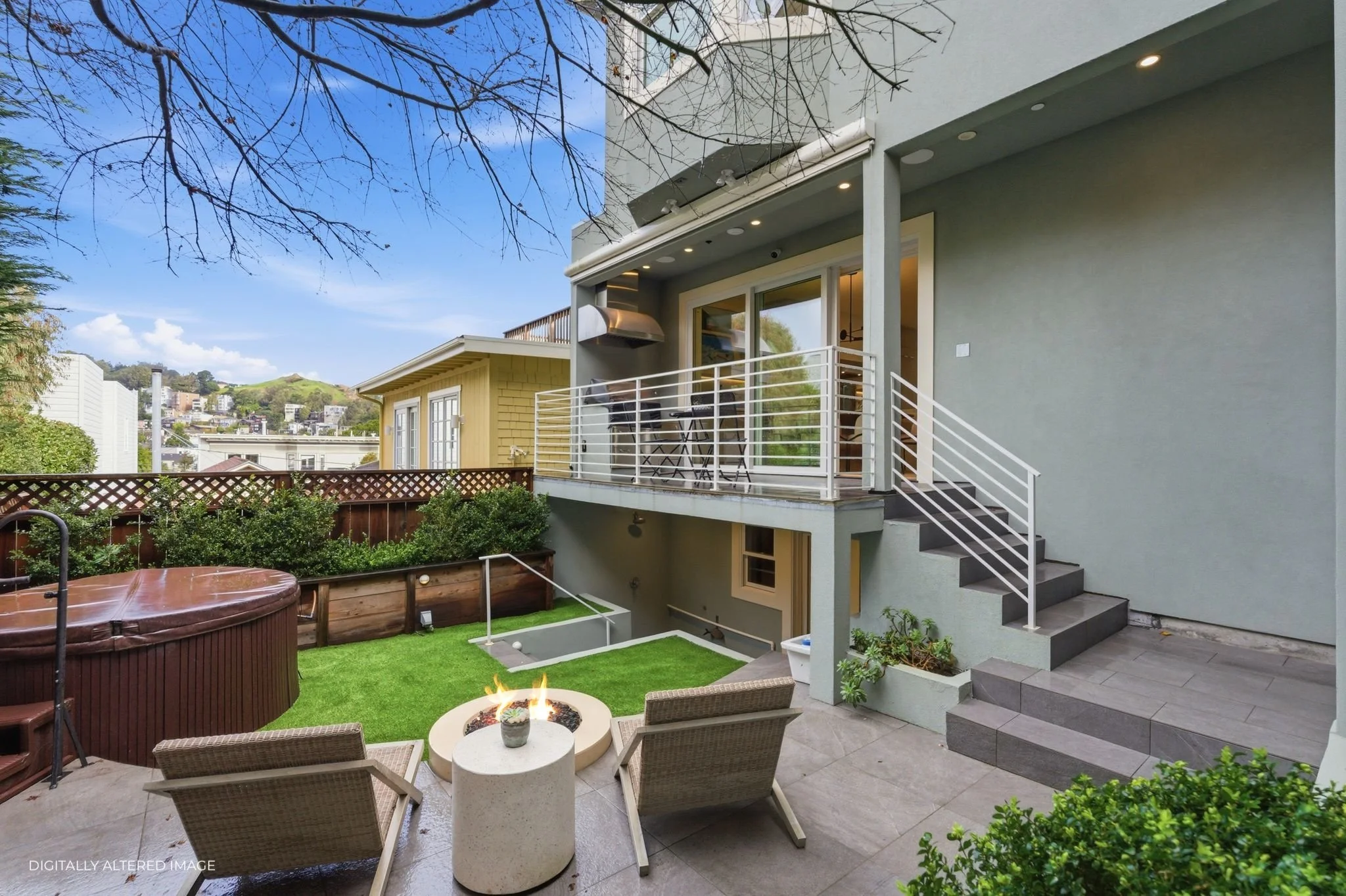 Outdoor view of a backyard with a patio, fire pit, chairs, a hot tub, a grassy area, and a two-story house with a balcony, steps, and greenery.