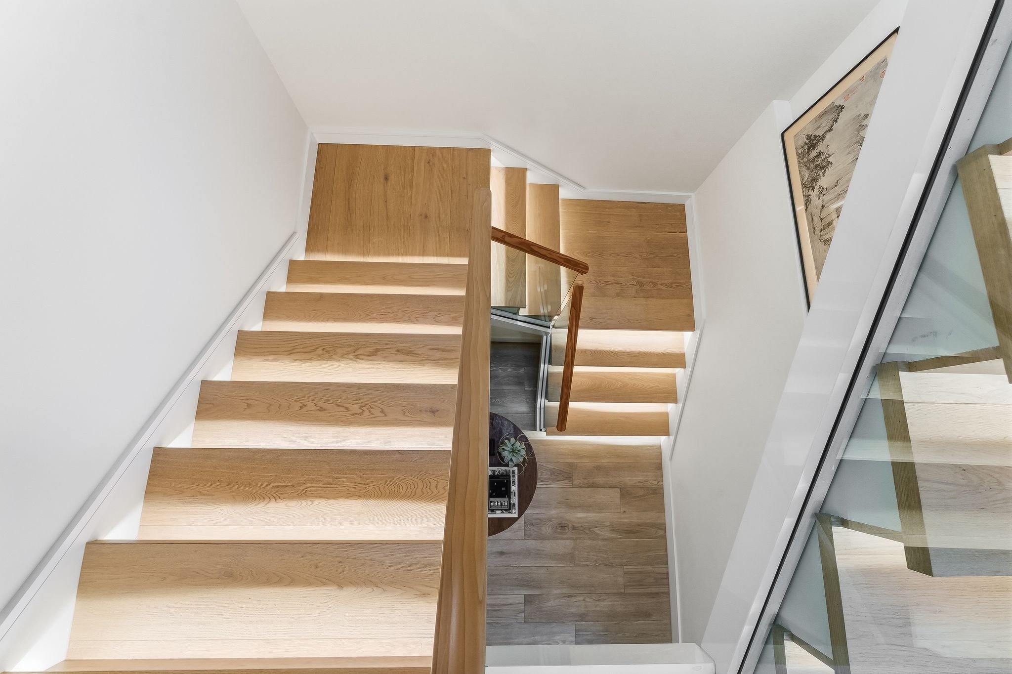 View of a wooden staircase from above, showing steps and a glass railing with wooden handrail in a modern home."