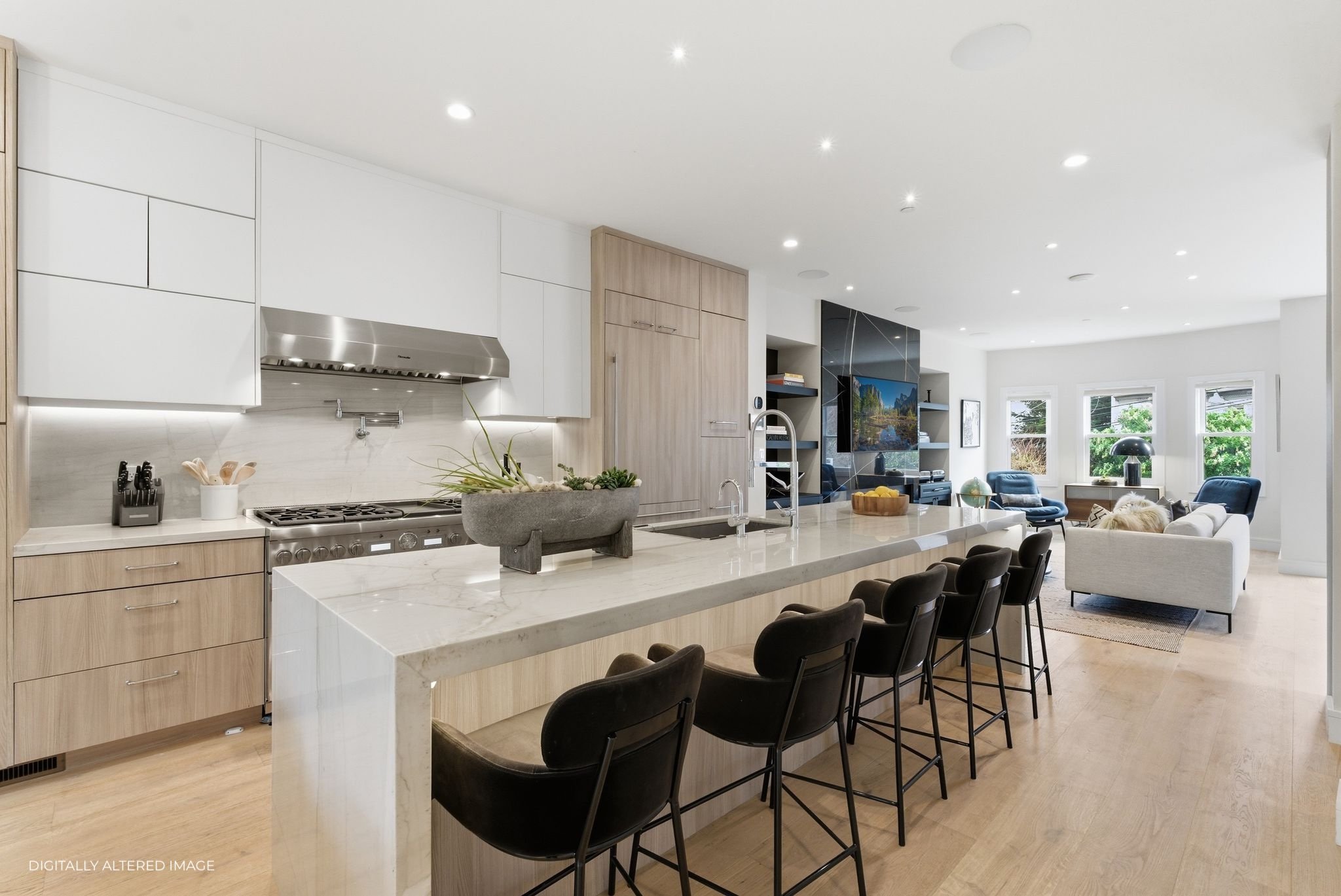 Modern open-concept kitchen and living area with white cabinetry, marble countertops, black chairs, and large windows with greenery outside.