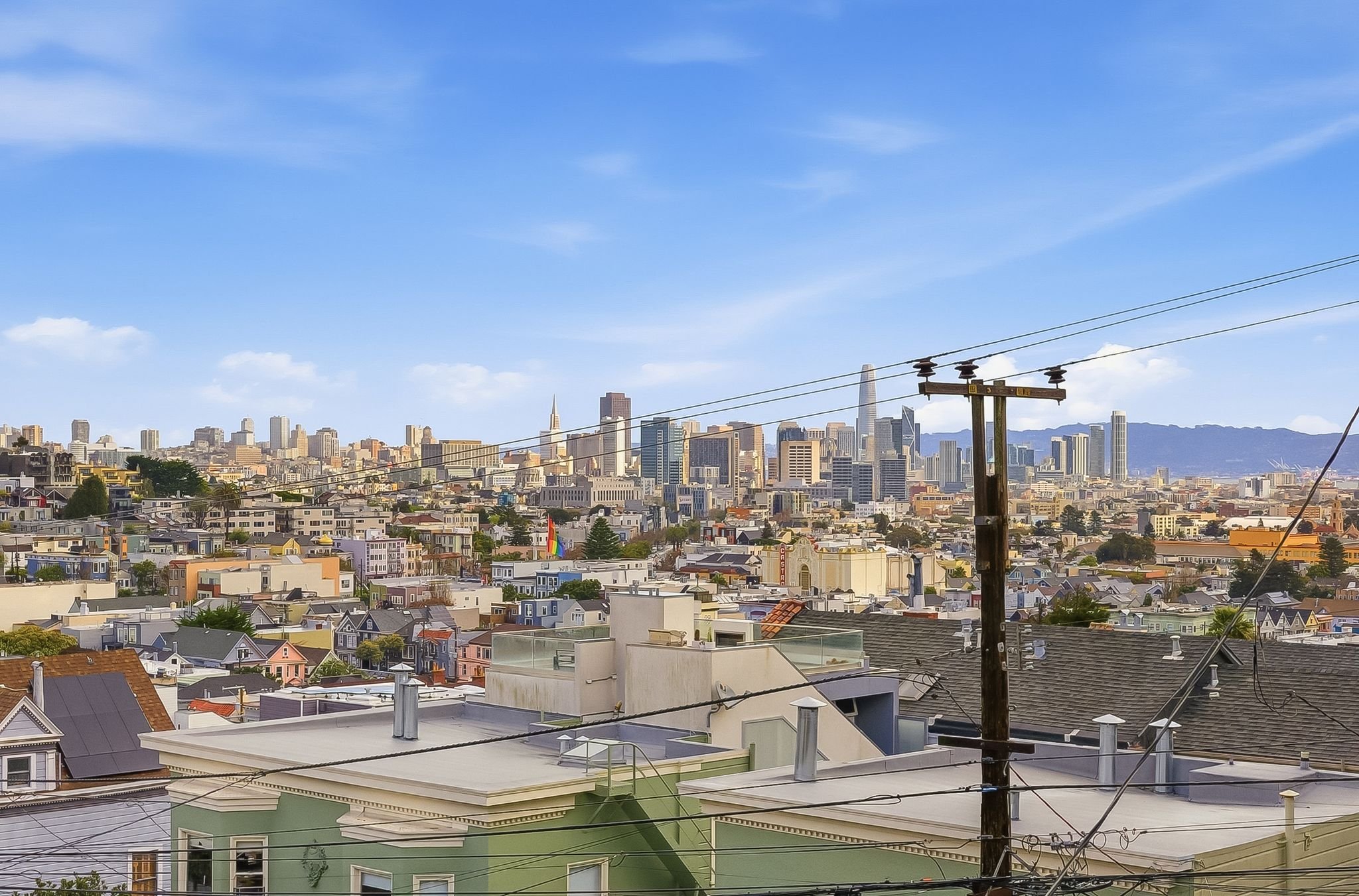 City skyline with tall buildings, clear blue sky, and utility poles and wires in the foreground.