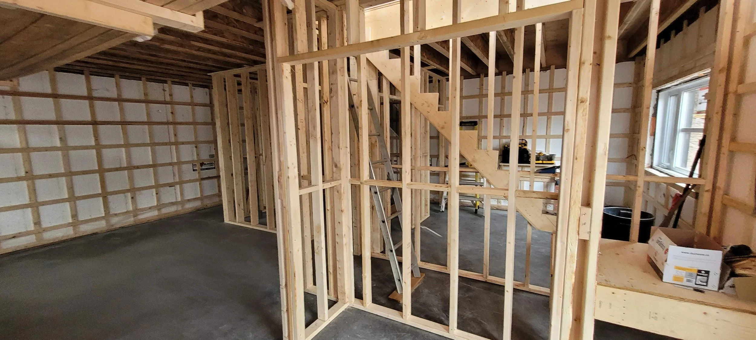 Interior of a house under construction with exposed wooden framing, staircase, window, and construction tools.