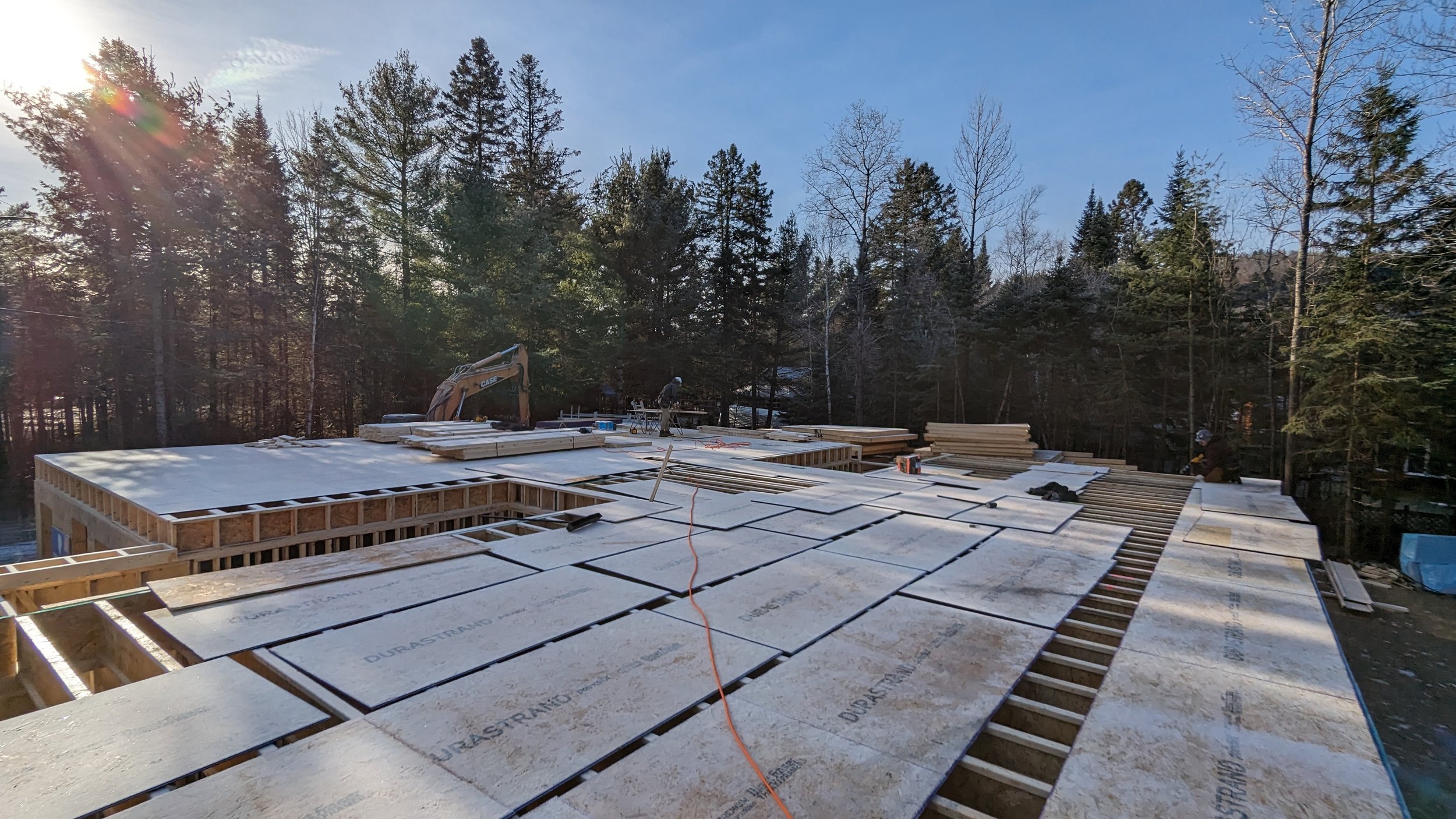 Construction workers installing insulation on the roof of a building under construction with a forest and blue sky in the background.