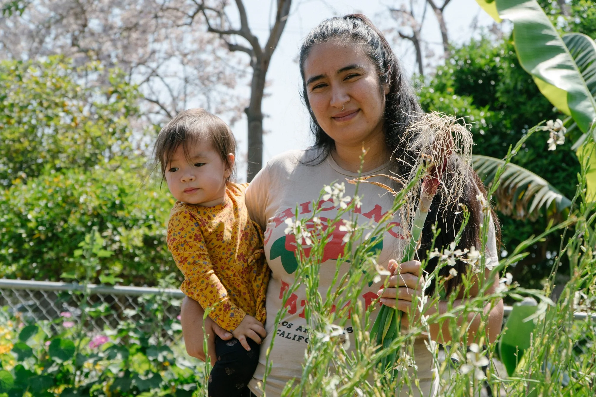 Photo of parent holding a bunch of green onions and a baby in the garden