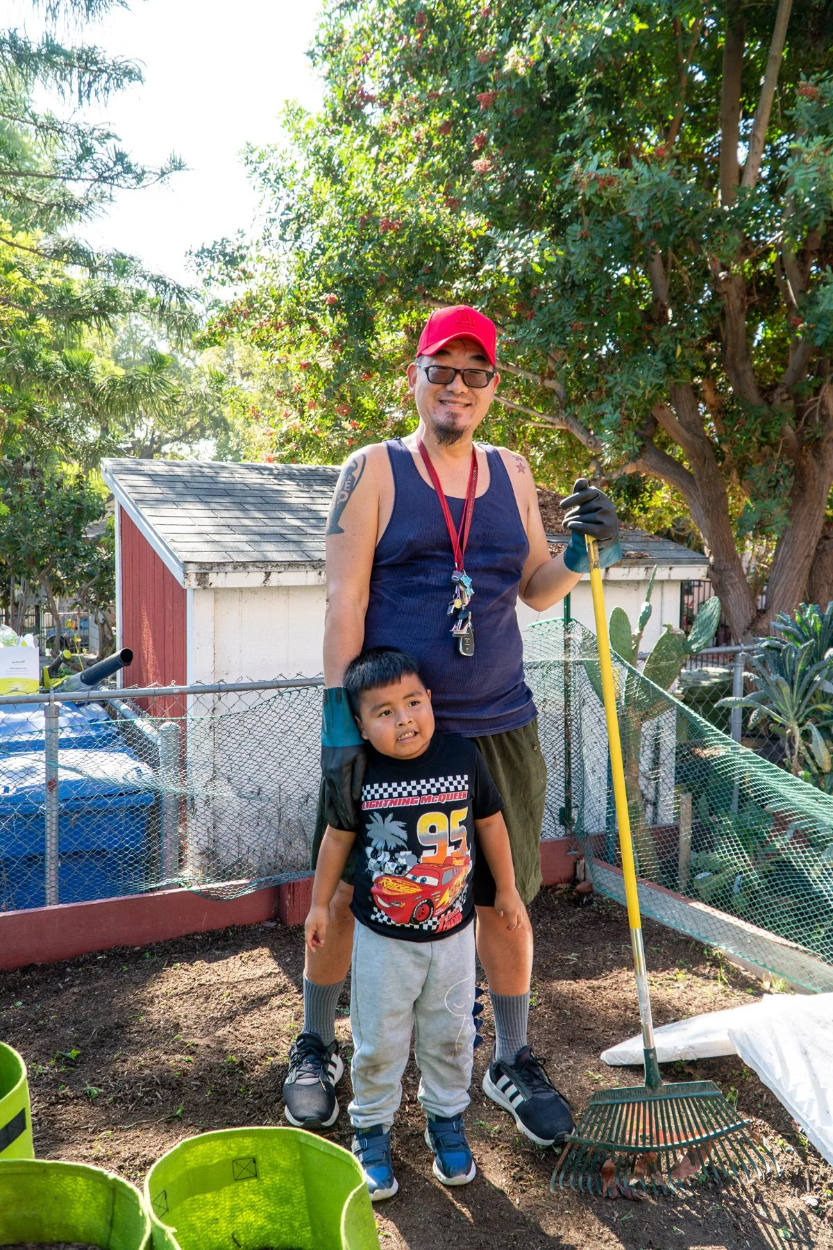 Photo of parent and child smiling while standing in a garden bed with a rake