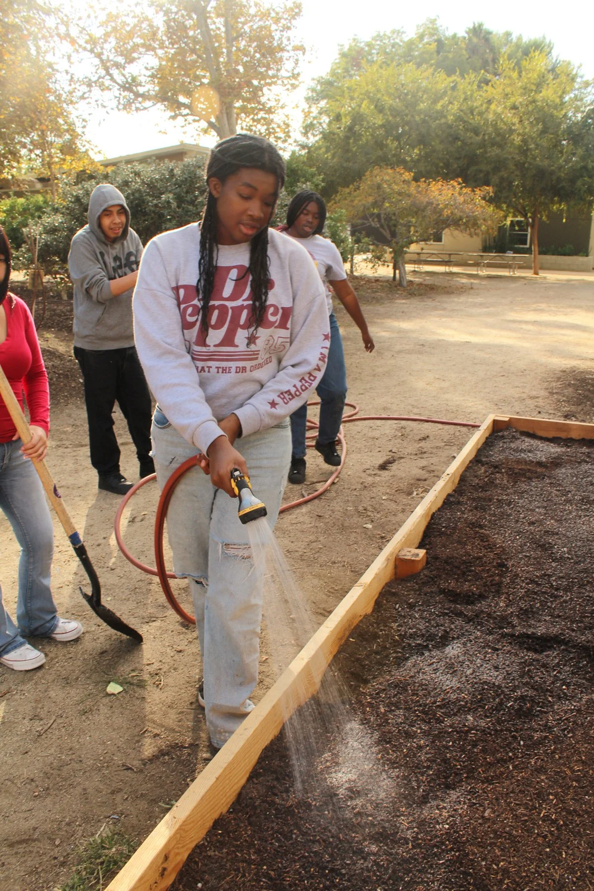 Photo of students in a garden with one student spraying a garden bed with a hose