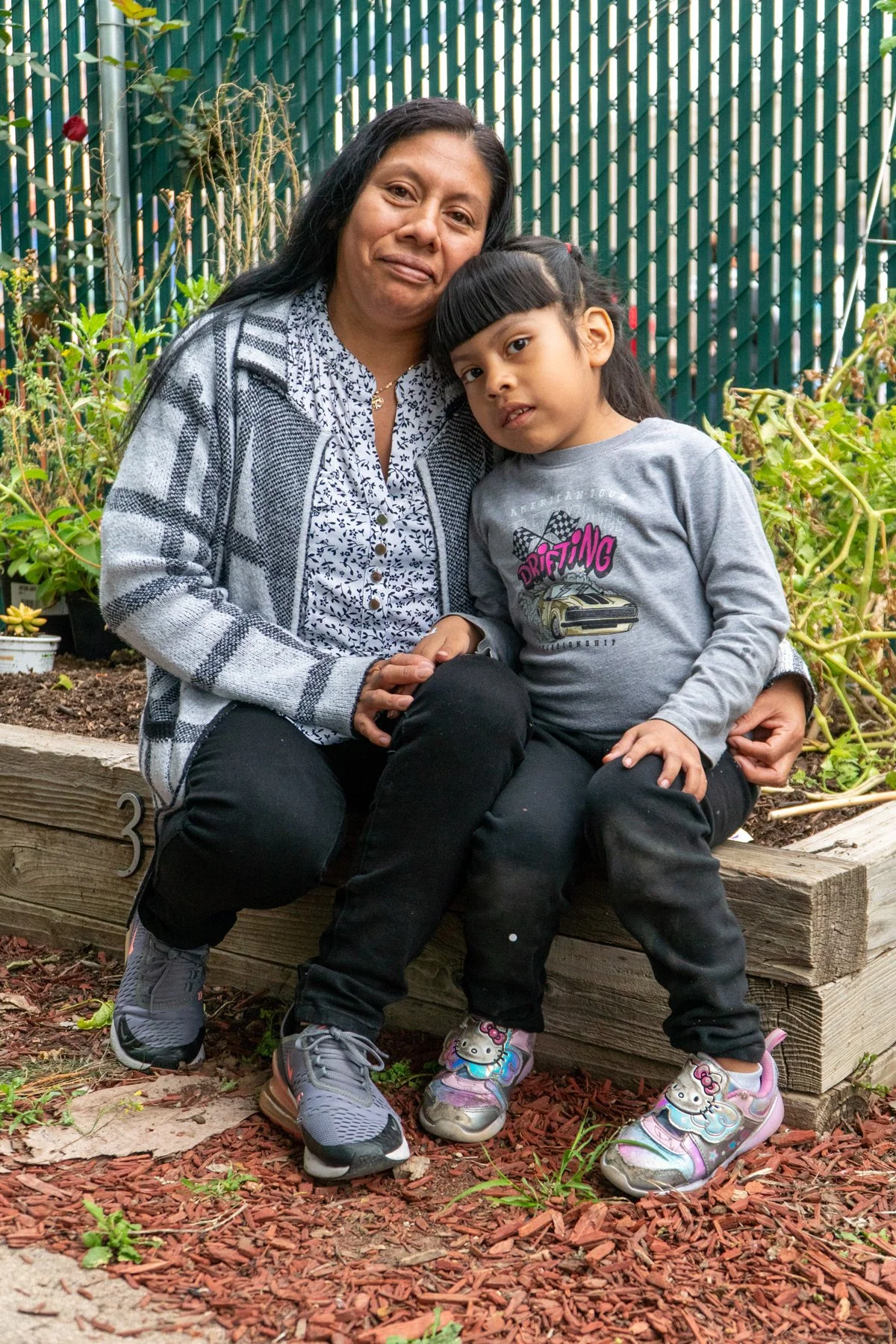 Photo of parent and young child sitting on a garden bed.