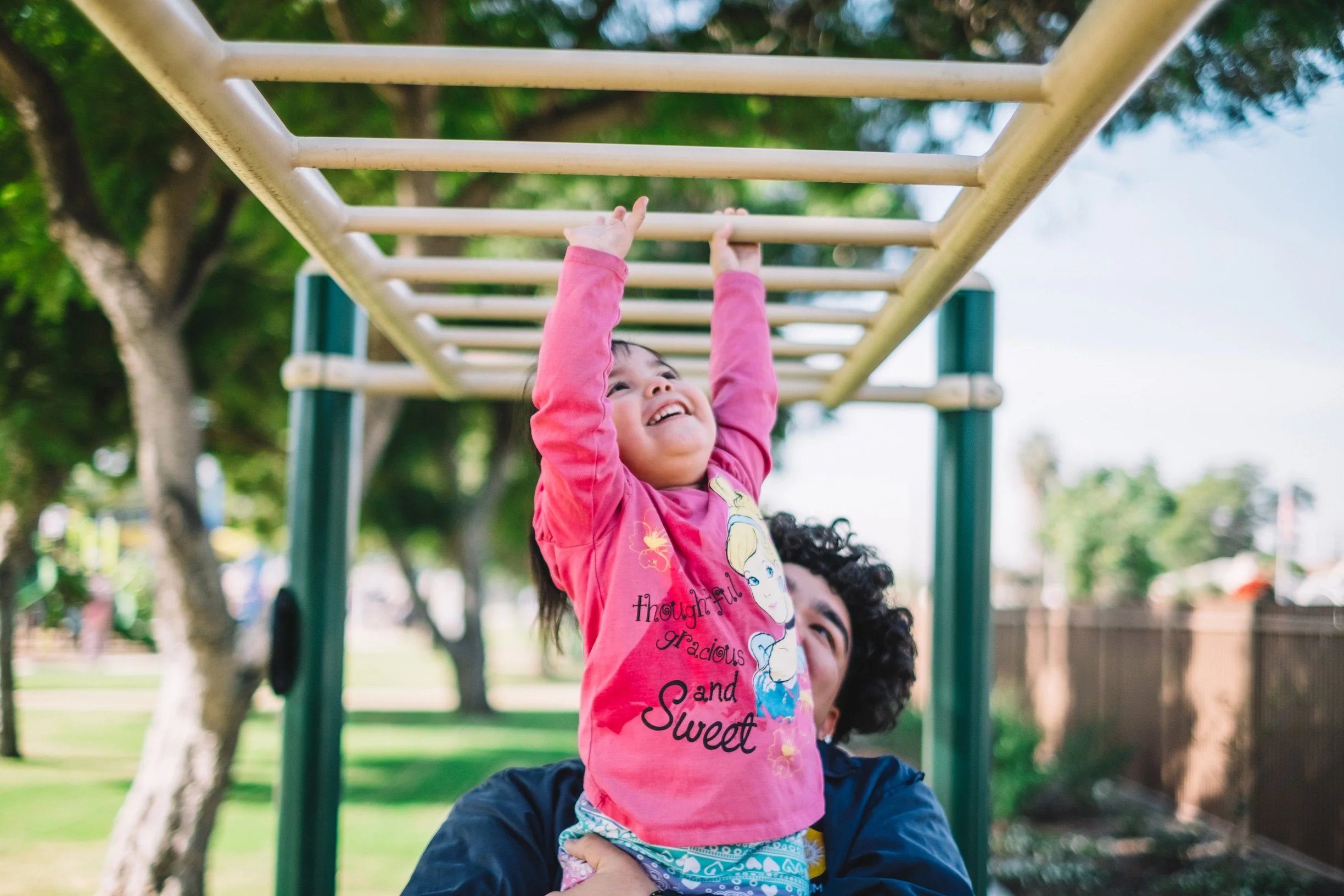 Photo of a parent holding a child climbing monkey bars at Jacaranda Park