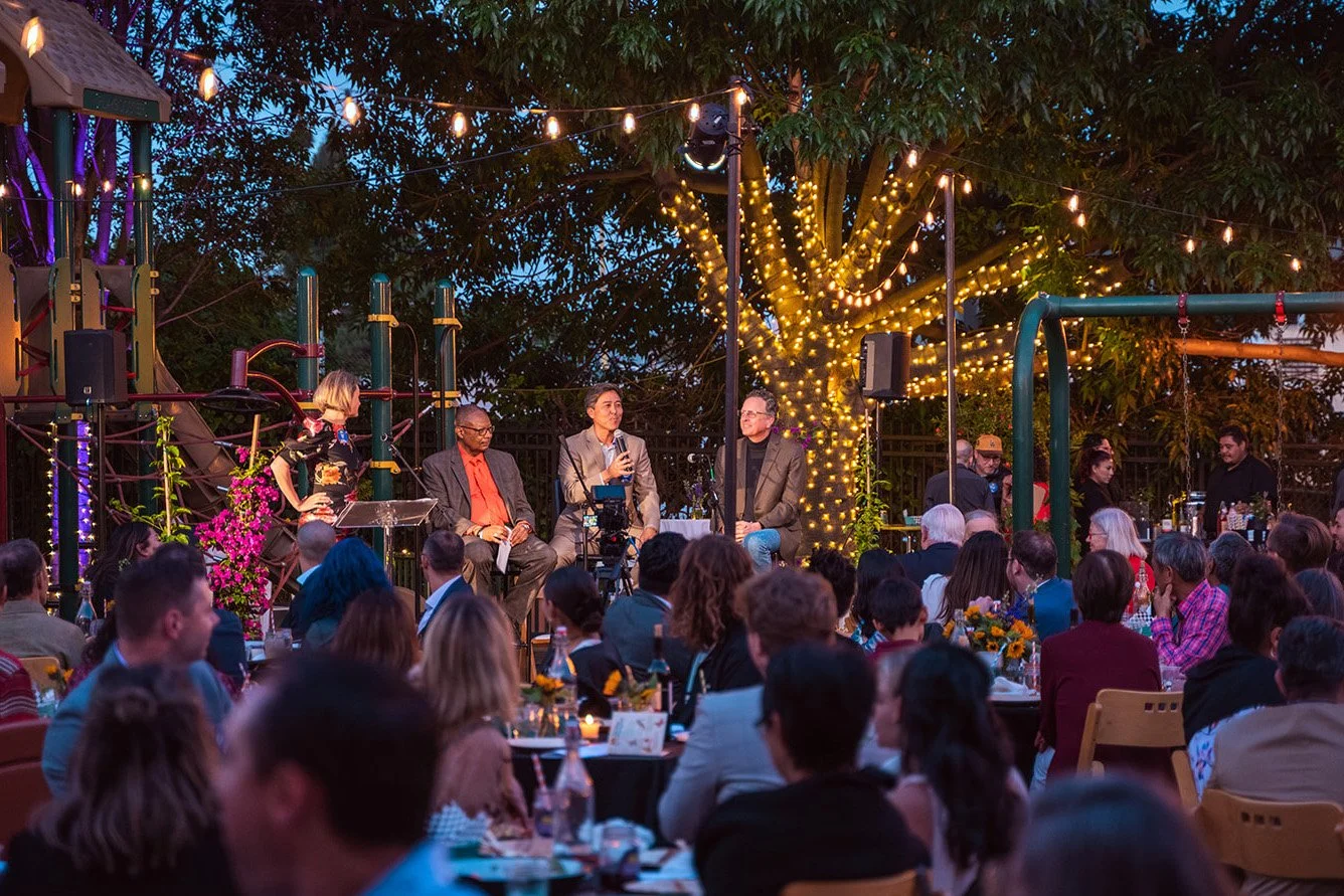 Photo of group of speakers in front of a lit-up park playground
