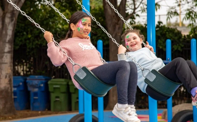 Photo of two children on the swings with their faces painted