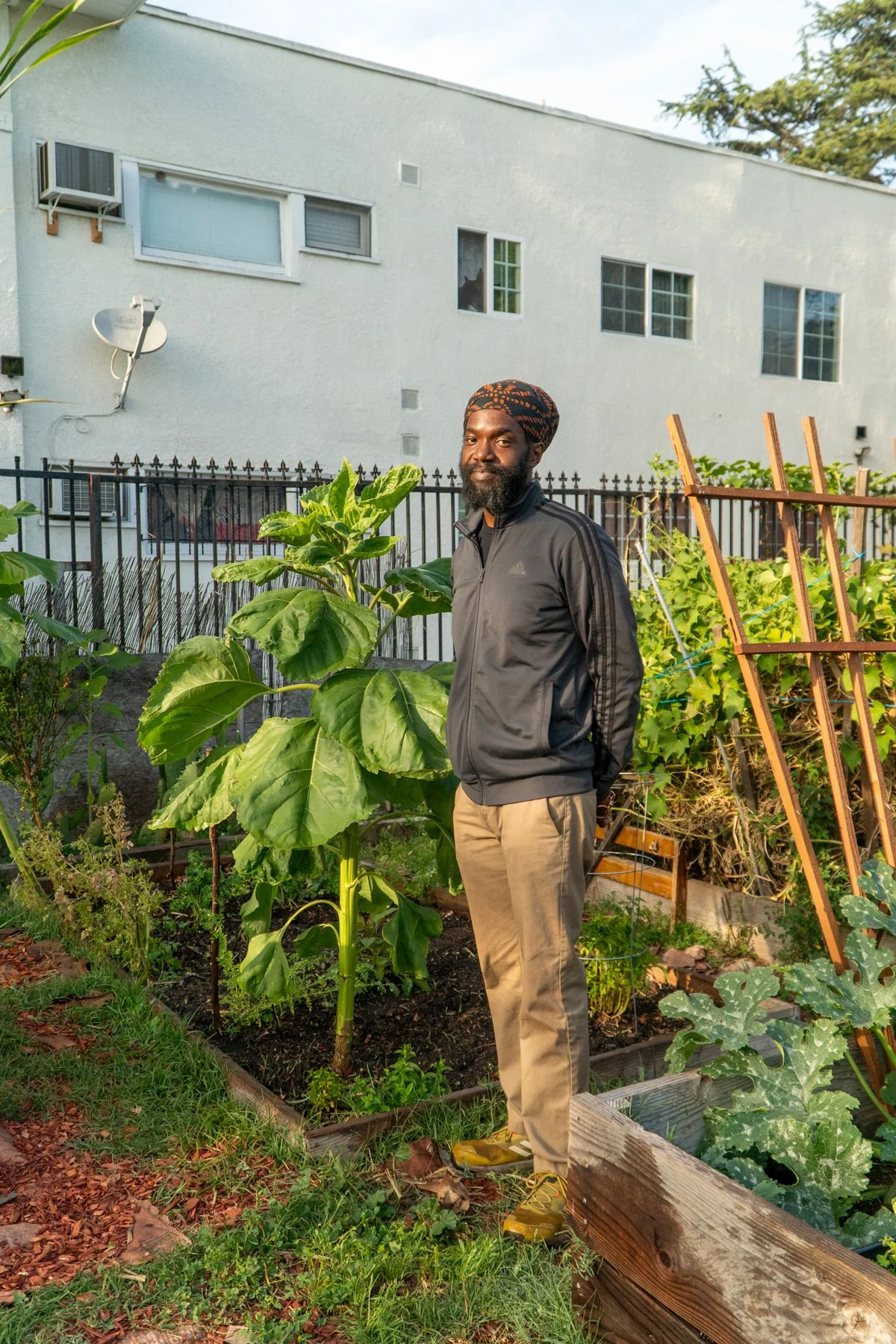 Photo of Chef Korby Benoit next to a tall plant amongst garden plots