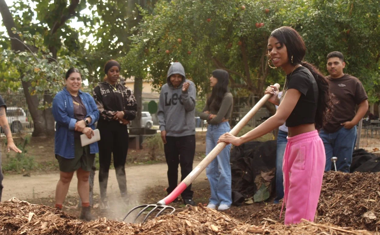 Photo of high school students in garden with one in the foreground raking soil