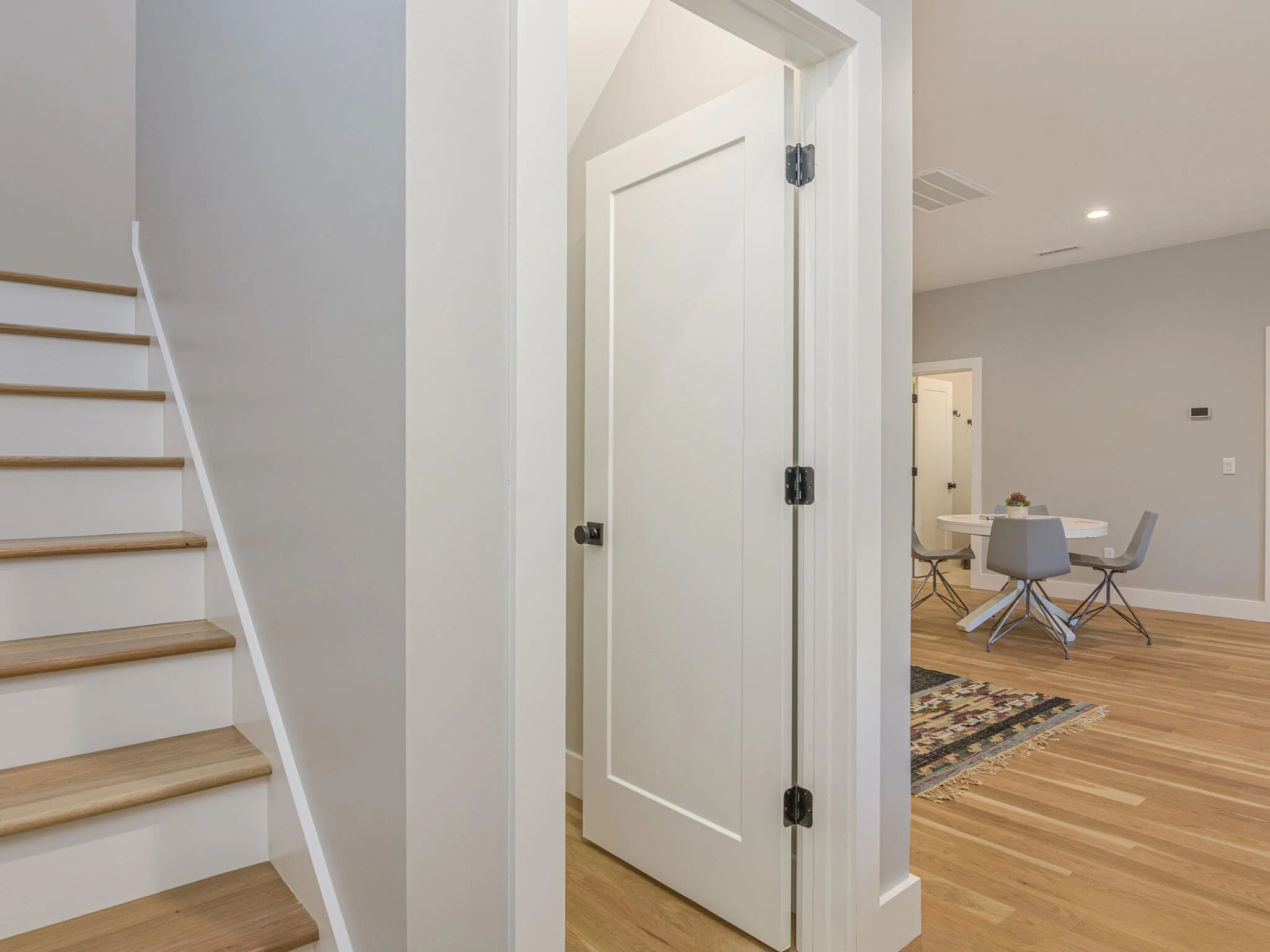 Interior of a modern home showing a staircase, a doorway, and part of the dining area with a round table and chairs.