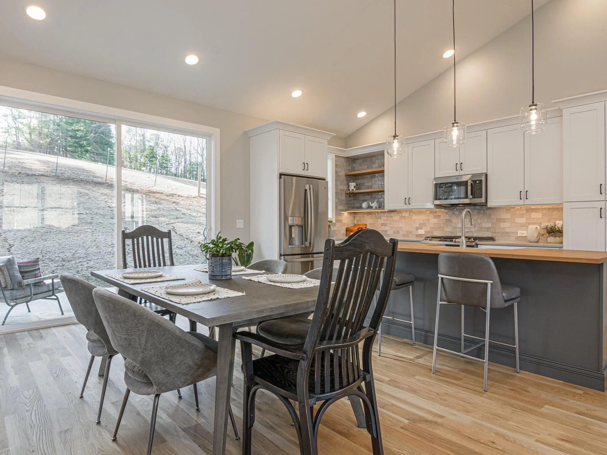 Modern open-concept kitchen and dining area with large glass sliding door, wooden dining table with six chairs, and pendant lighting.