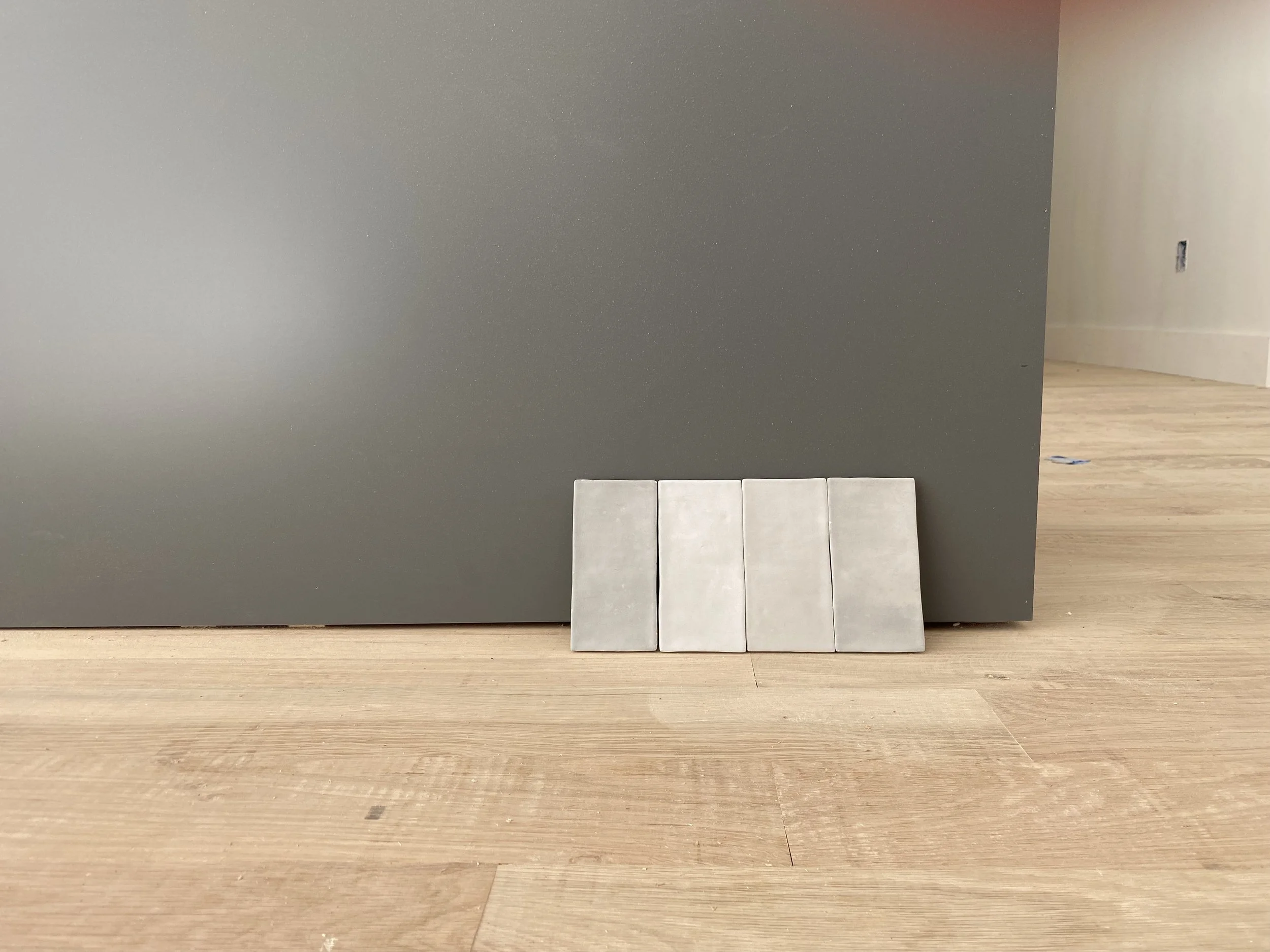 Four small tiles or panels leaning against a gray wall on a wooden floor.