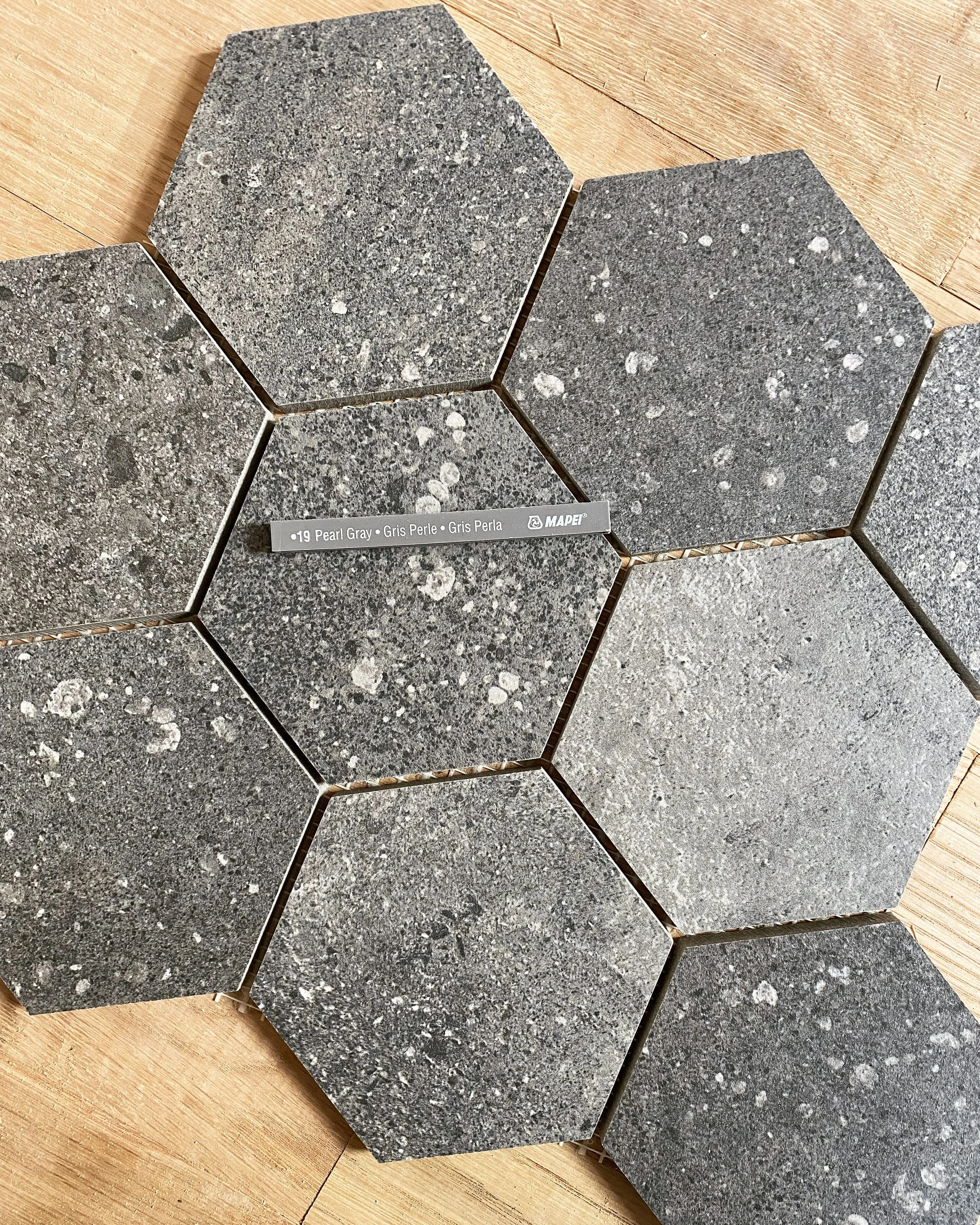 Seven hexagonal gray stone tiles with speckled pattern on a wooden floor, labeled 'Pearl Gray'.
