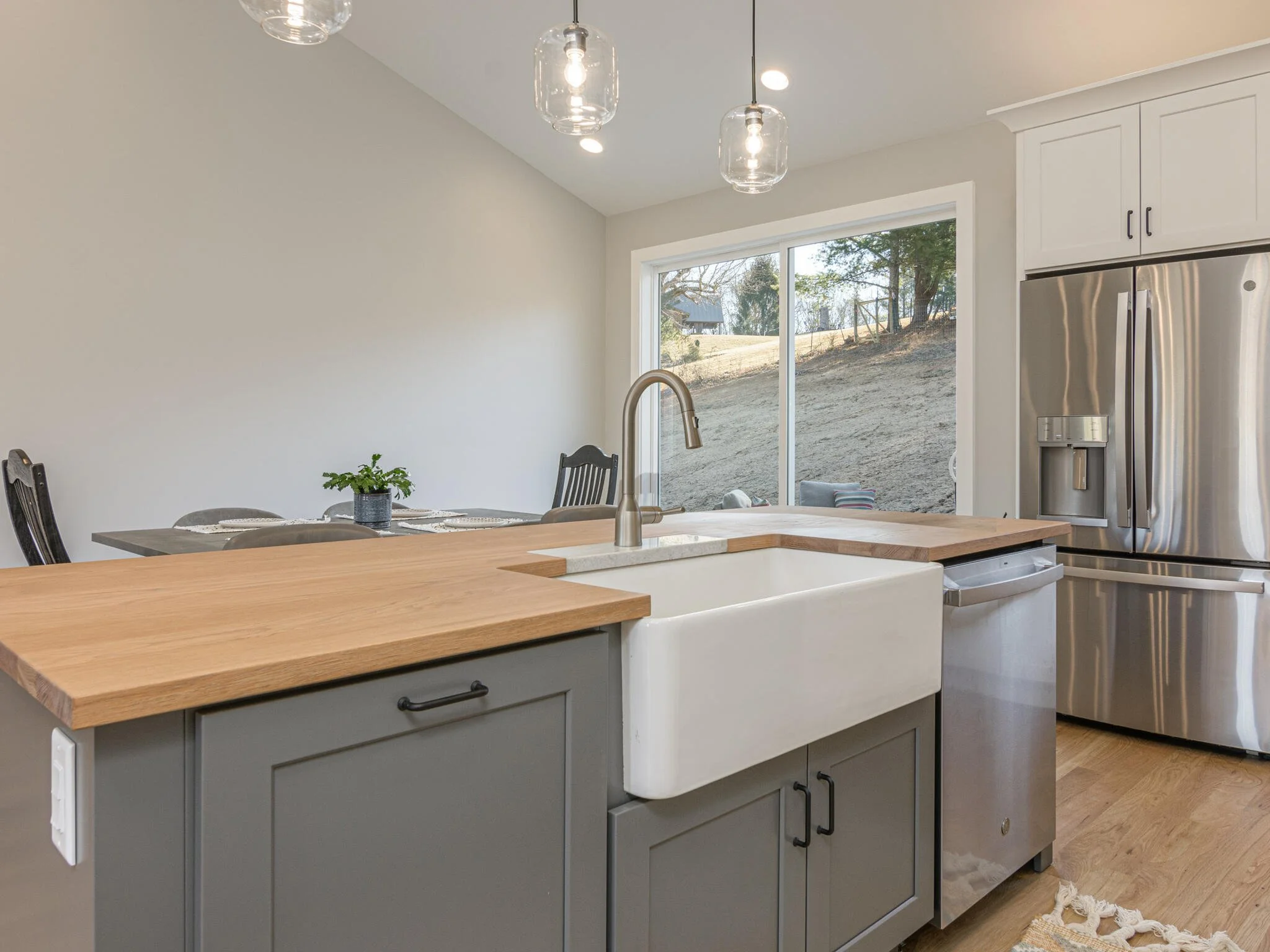Modern kitchen with a large farmhouse sink, wooden countertop, stainless steel refrigerator, and a sliding glass door leading outside.