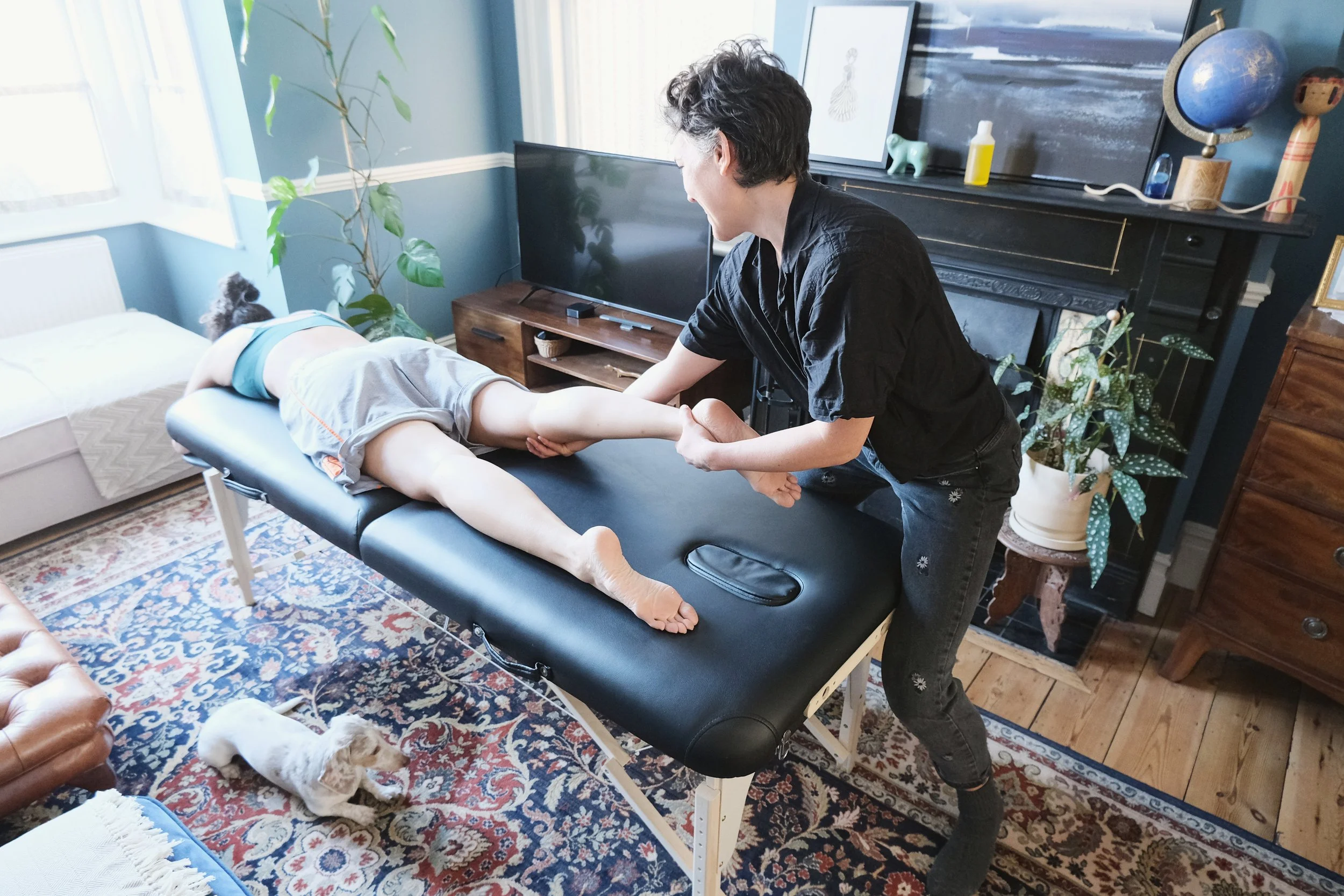 Jackie giving a person a massage therapy on a massage table in their living room
