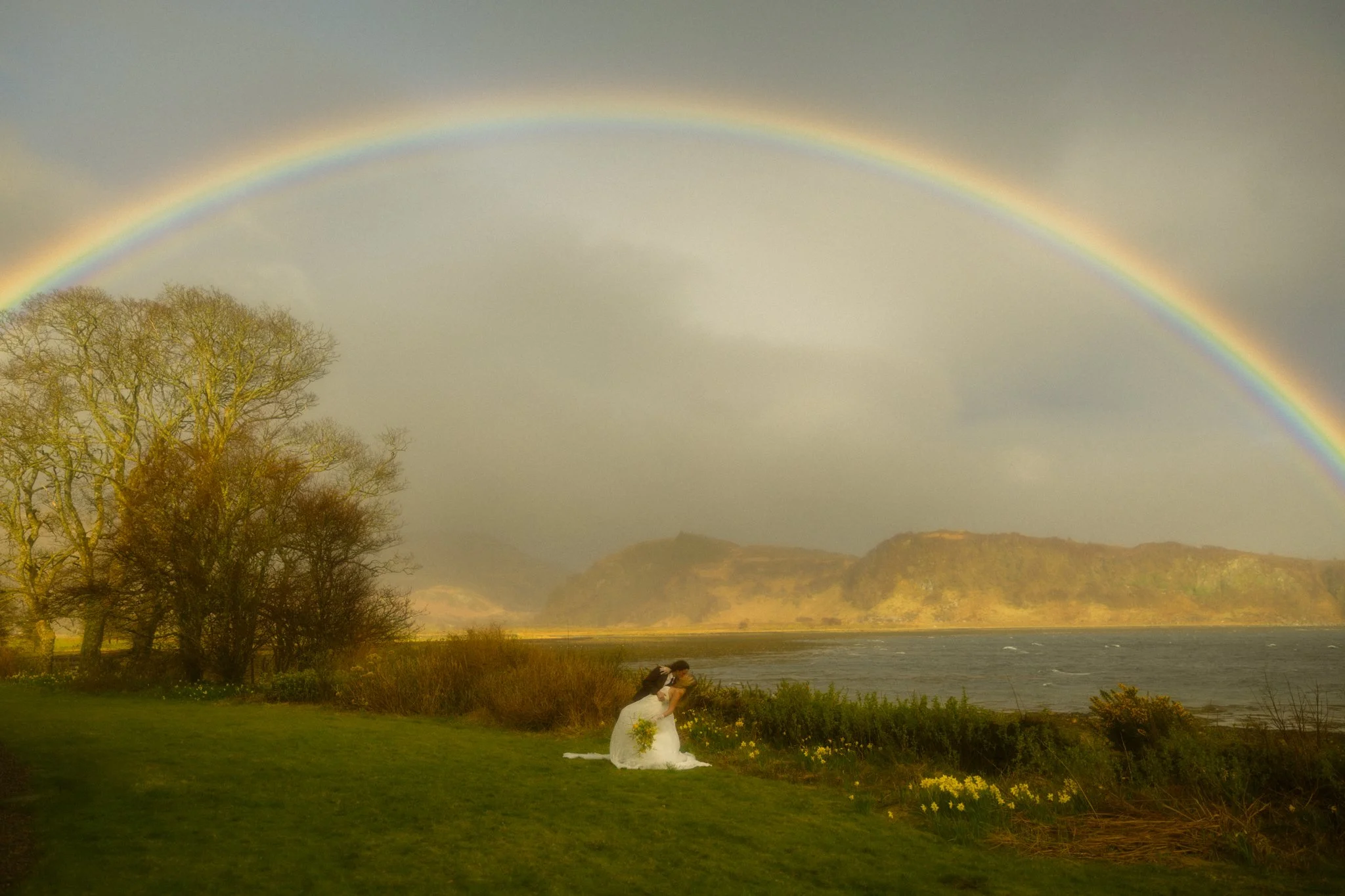 an elopement couple kissing along Loch Alsh under a vibrant rainbow in the Scottish Highlands