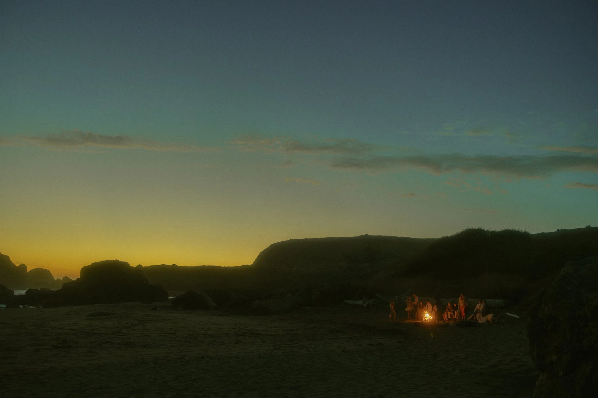 elopement couple and their guests celebrating around a beach campfire at sunset