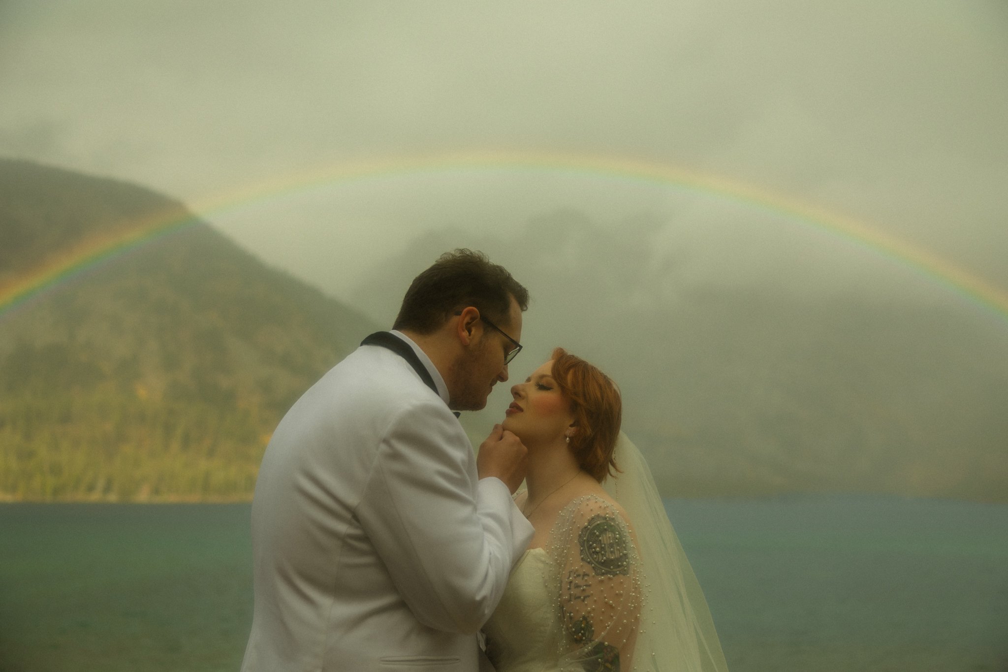 an elopement couple leaning in for a kiss under a rainbow in Grand Teton National Park