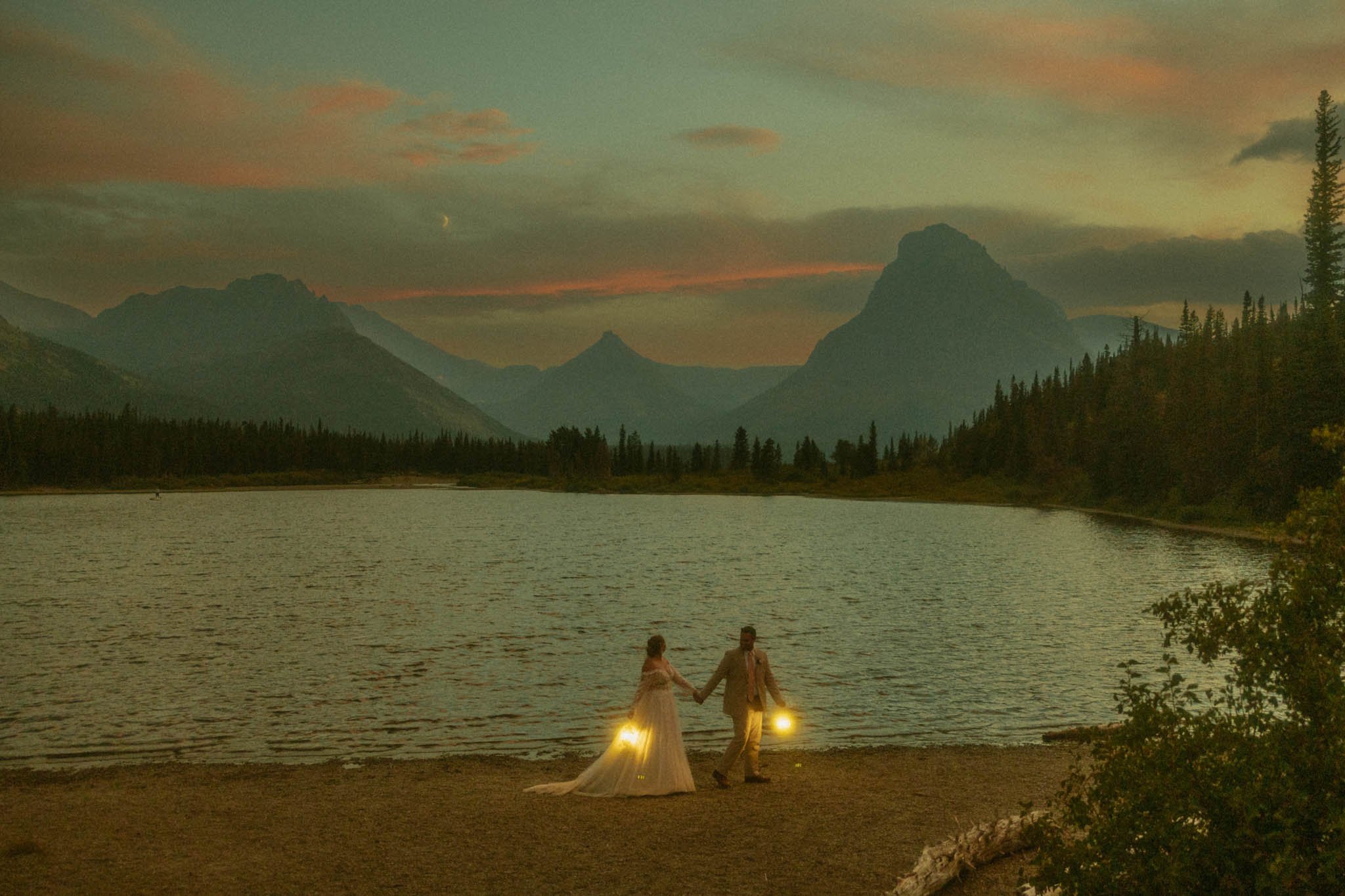 and elopement couple walking along Two Medicine Lake with lanterns in Glacier National Park
