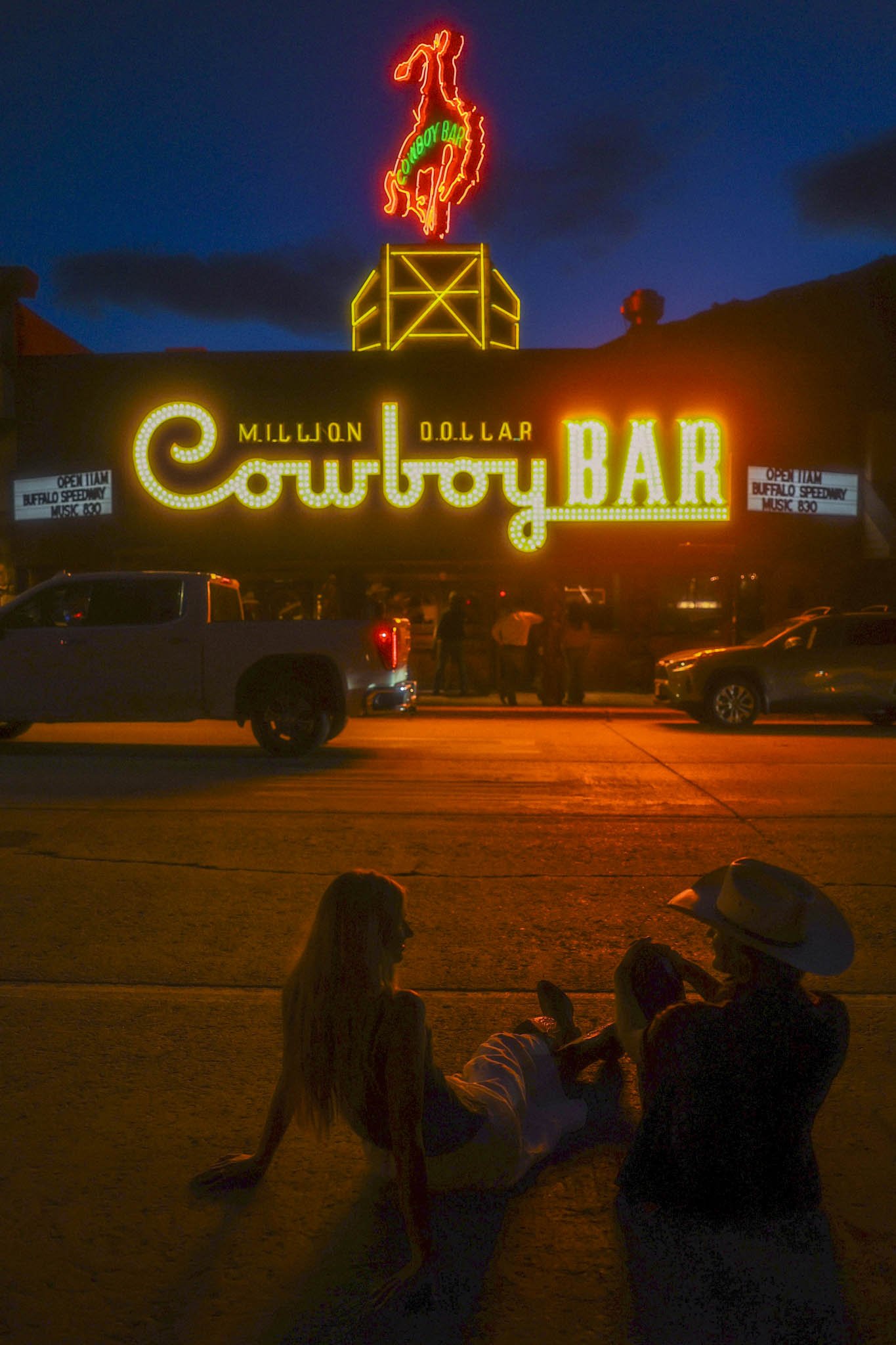 an elopement couple sitting on the ground outside Million Dollar Cowboy Bar at night