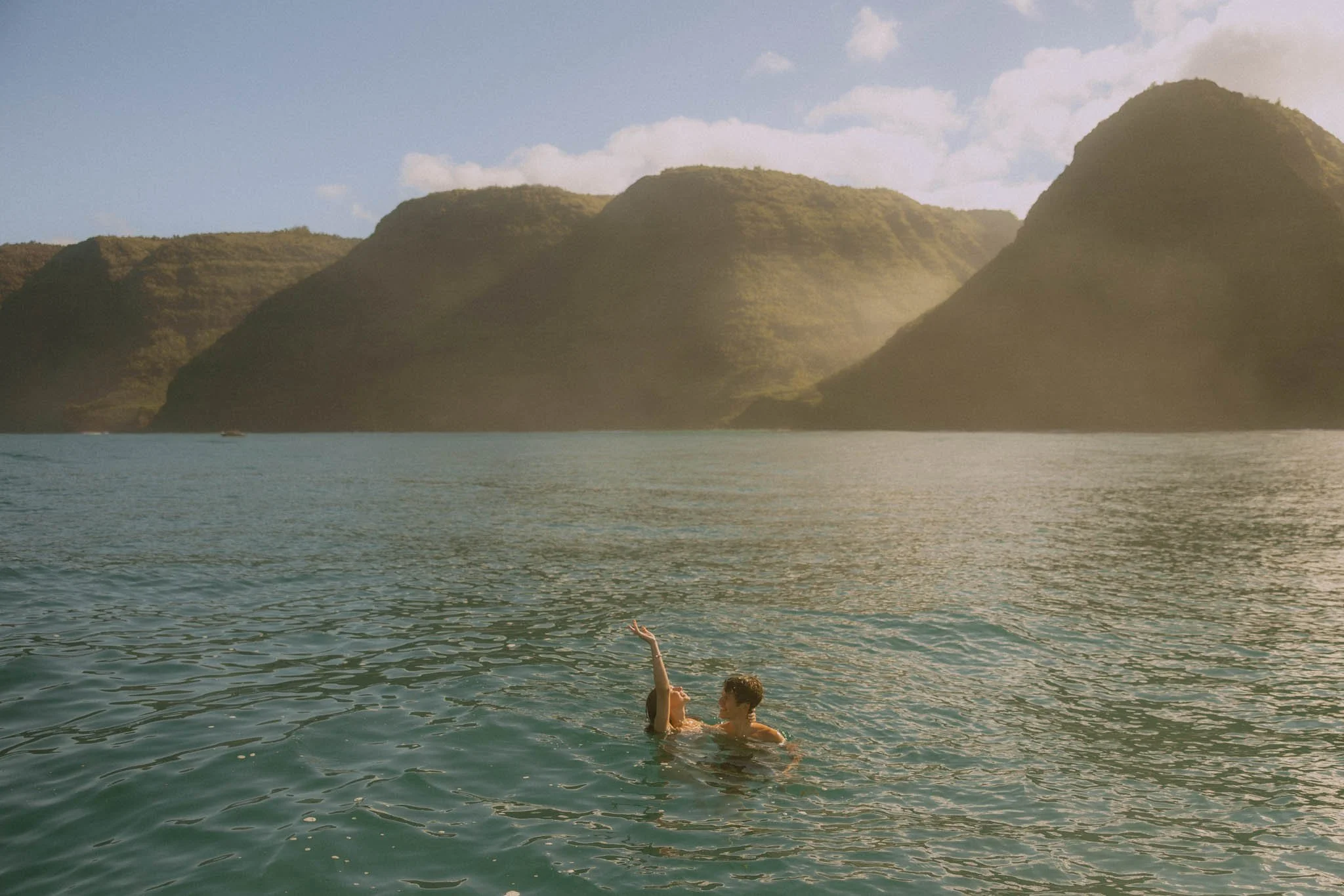 an elopement couple swimming along the Na Pali Coast in Kauai after their ceremony on a private boat