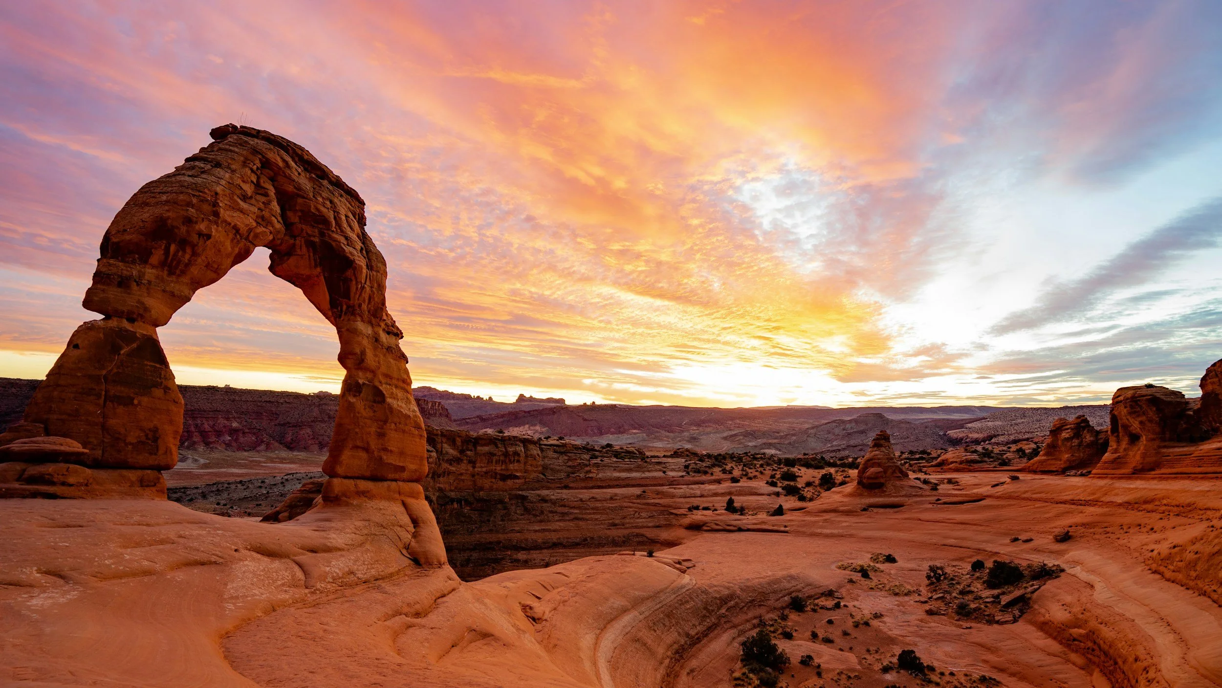 a landscape photo of Delicate Arch in Arches National Park located in Moab, Utah at sunset