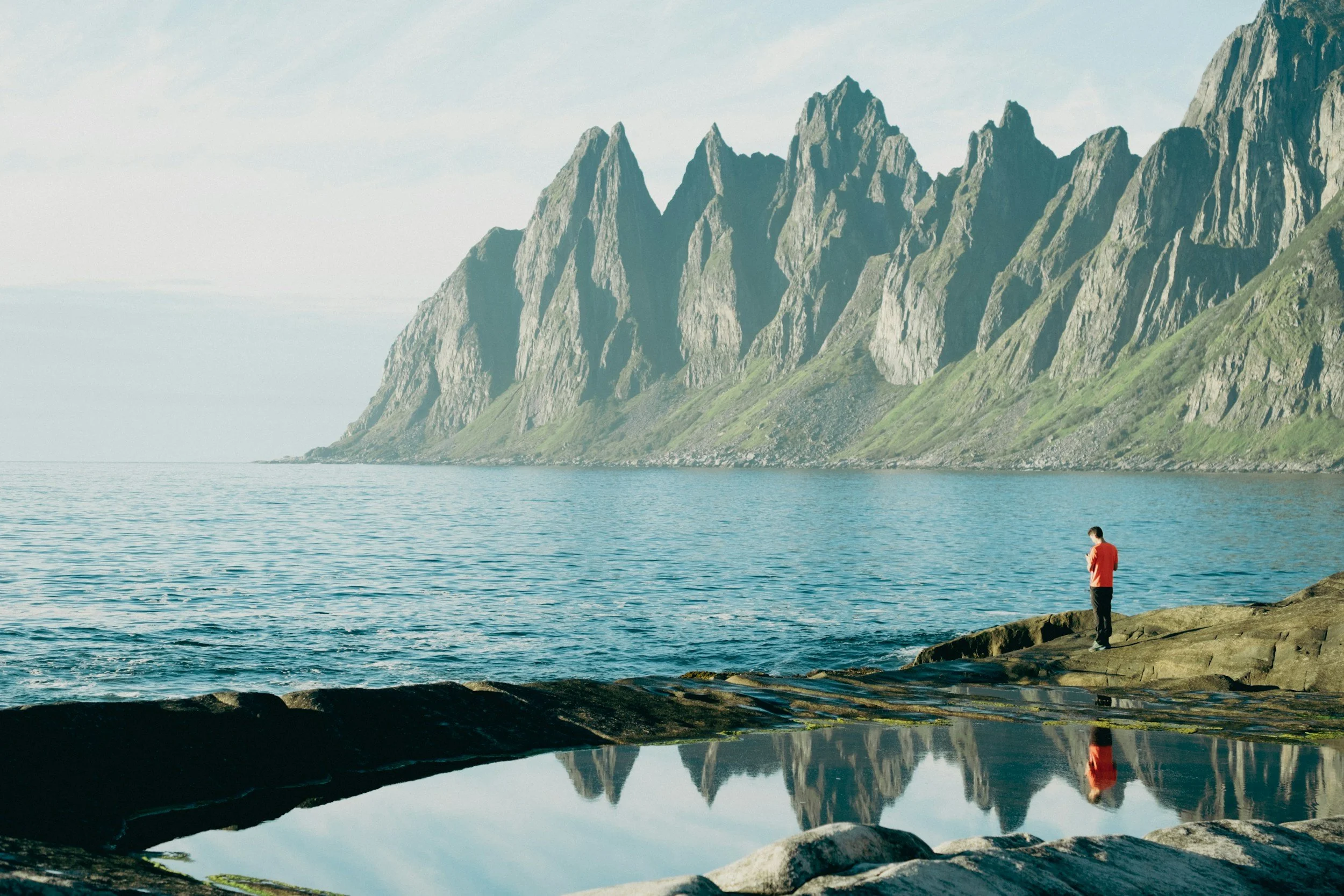 a person standing along a coastline with jagged mountains in the distance in Senja, Norway