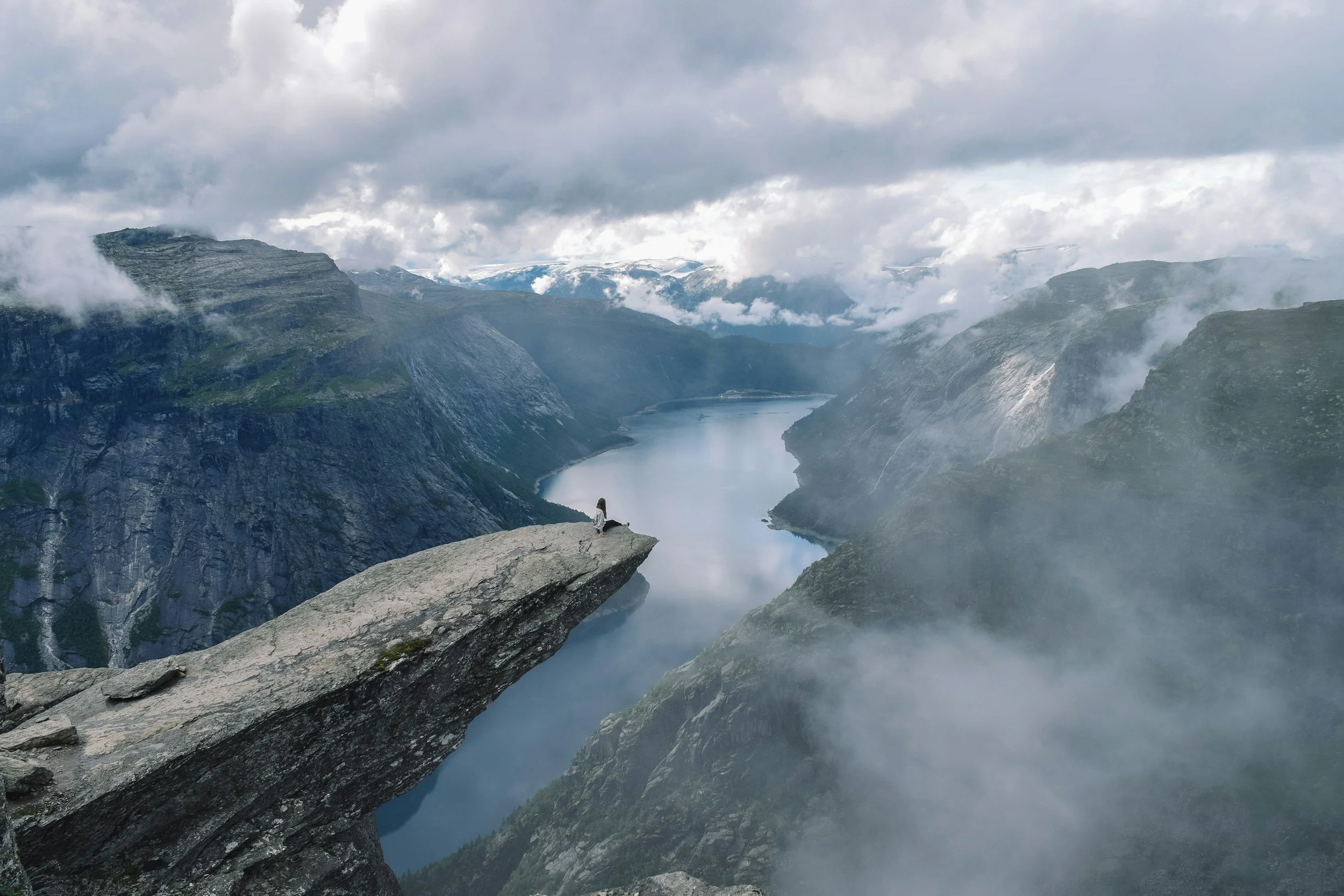 a landscape with a tiny person standing at the cliff edge at Trolltunga in Norway