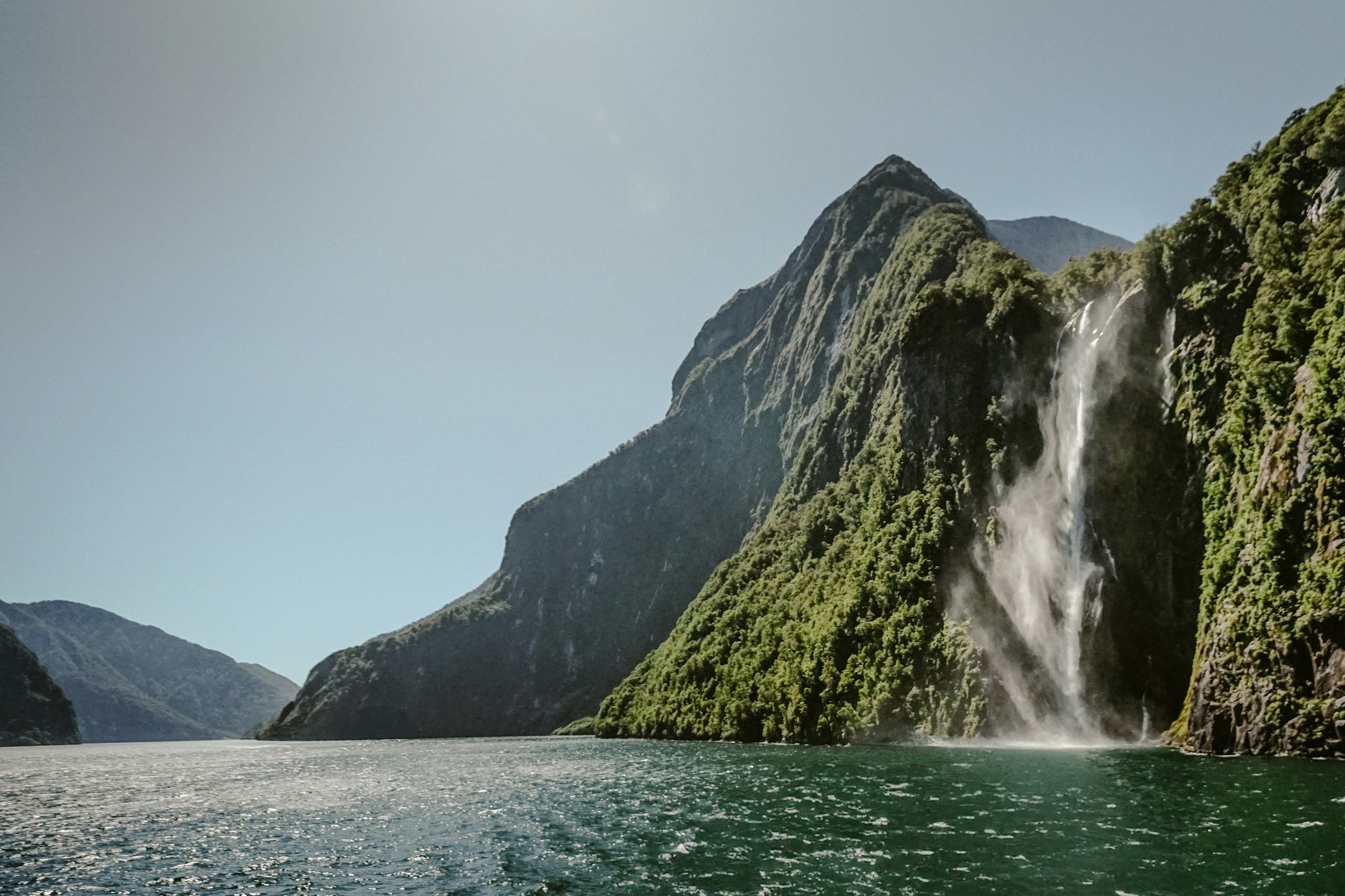 a landscape photo of a waterfall falling into the Milford Sound in New Zealand