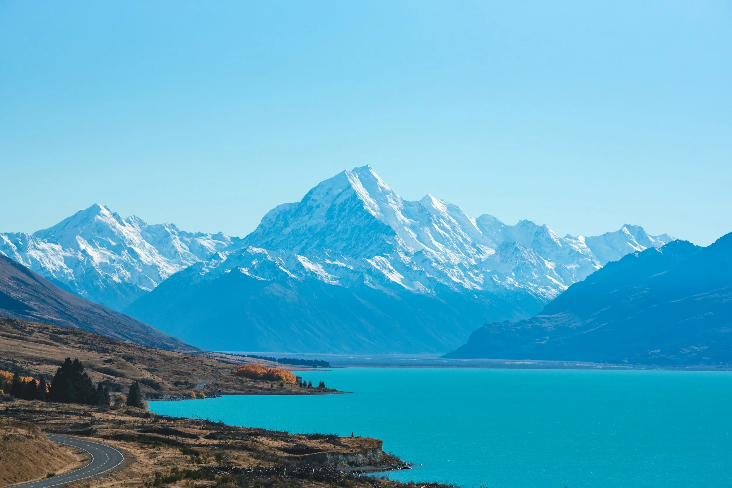 a landscape photo of a bright blue alpine lake with mountains in the distance in New Zealand