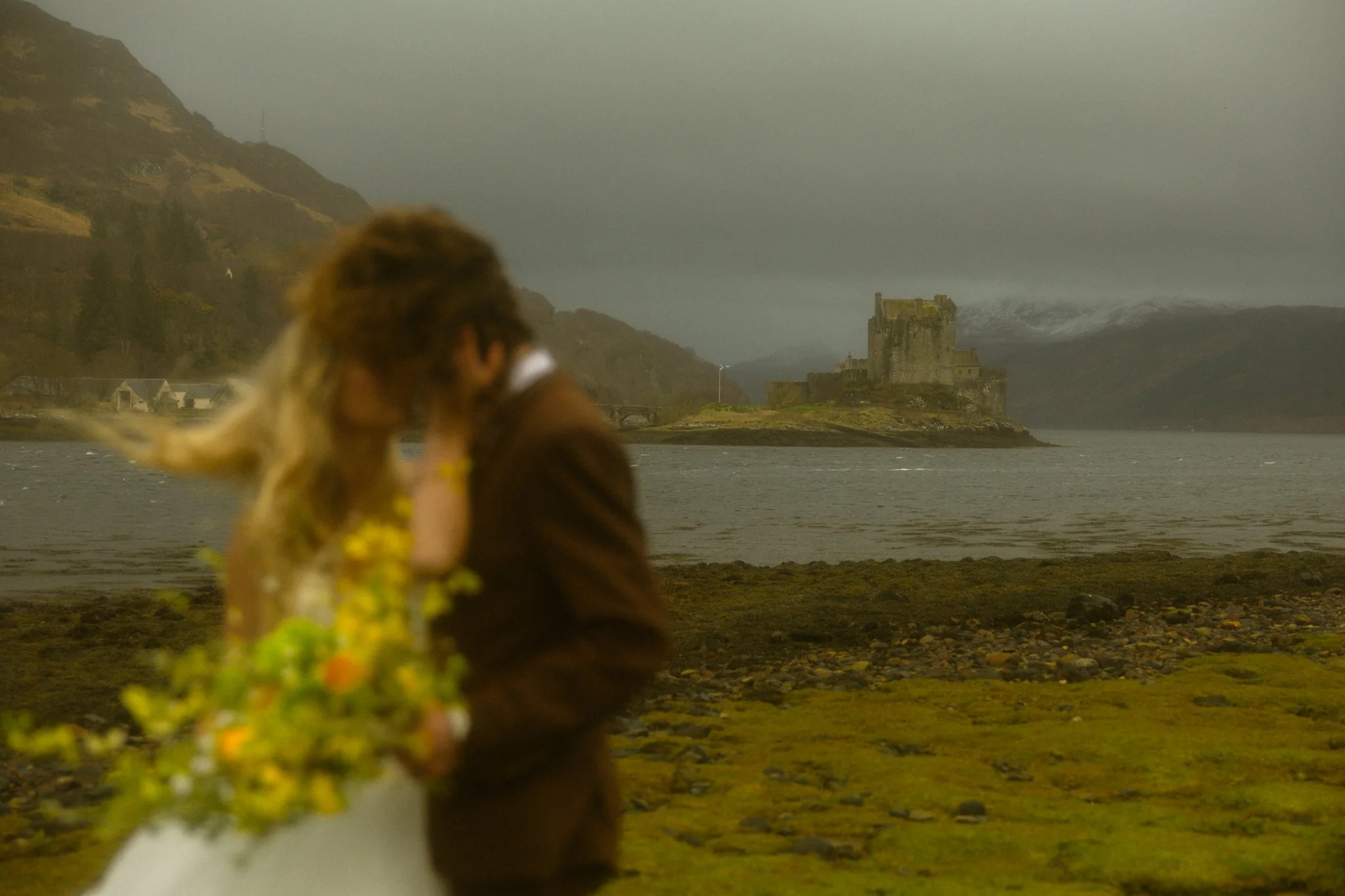 a couple kissing on their elopement at a lake with a castle in the background in Scotland