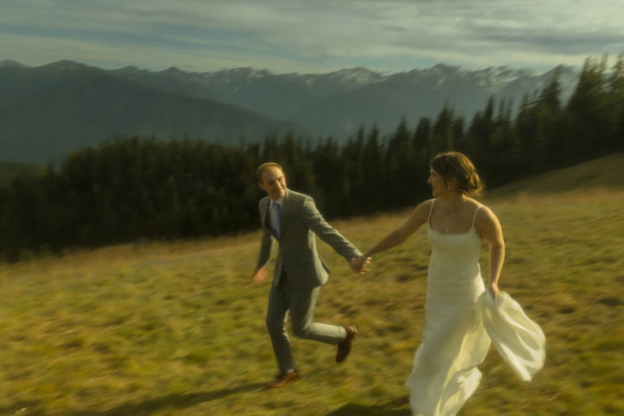 a wedding couple running in a field with mountains in the distance at Hurricane Ridge in Olympic National Park