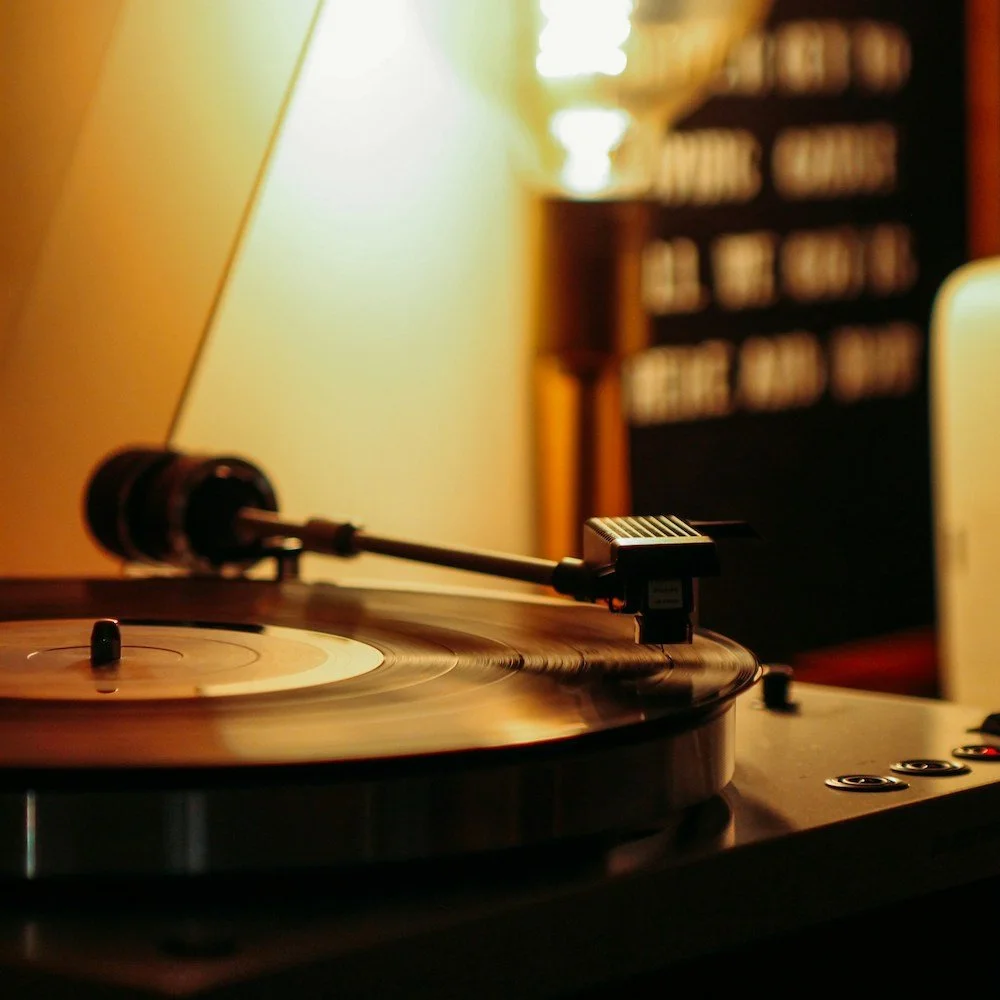 A close-up of a vinyl record player with a spinning record and tonearm, in a softly lit room.