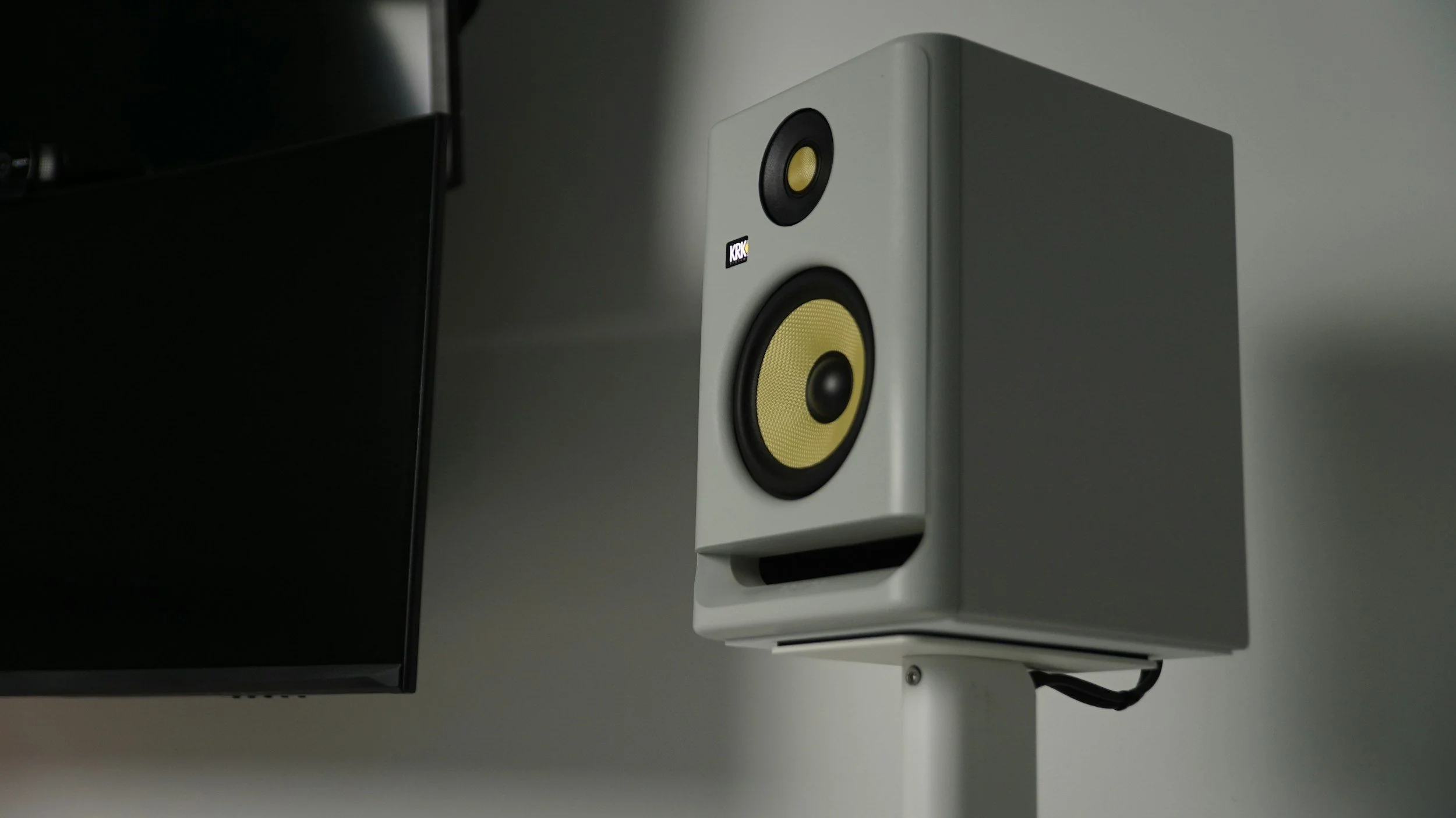 A white studio monitor speaker with yellow driver cones mounted on a stand.