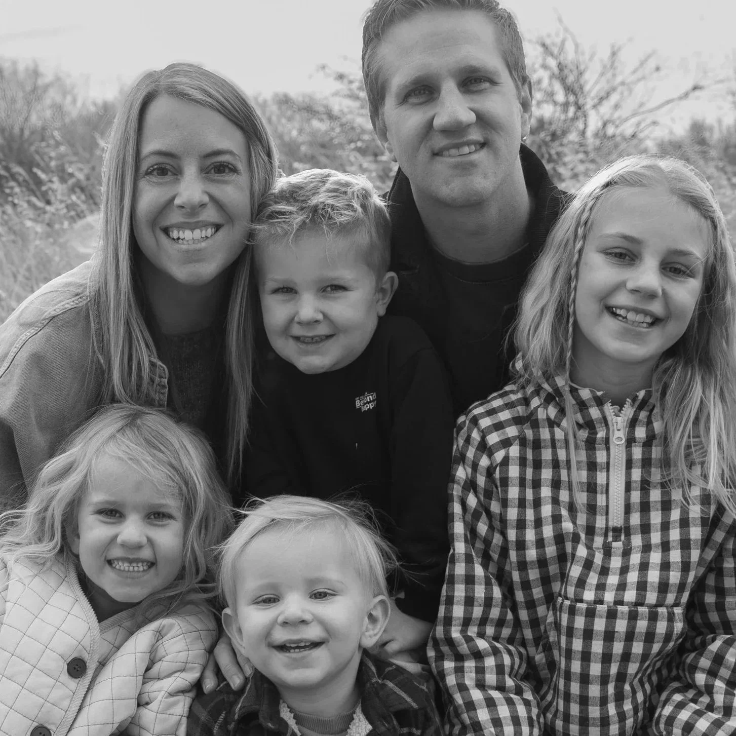 A black and white photo of a family of seven outdoors, smiling and posing for the camera.