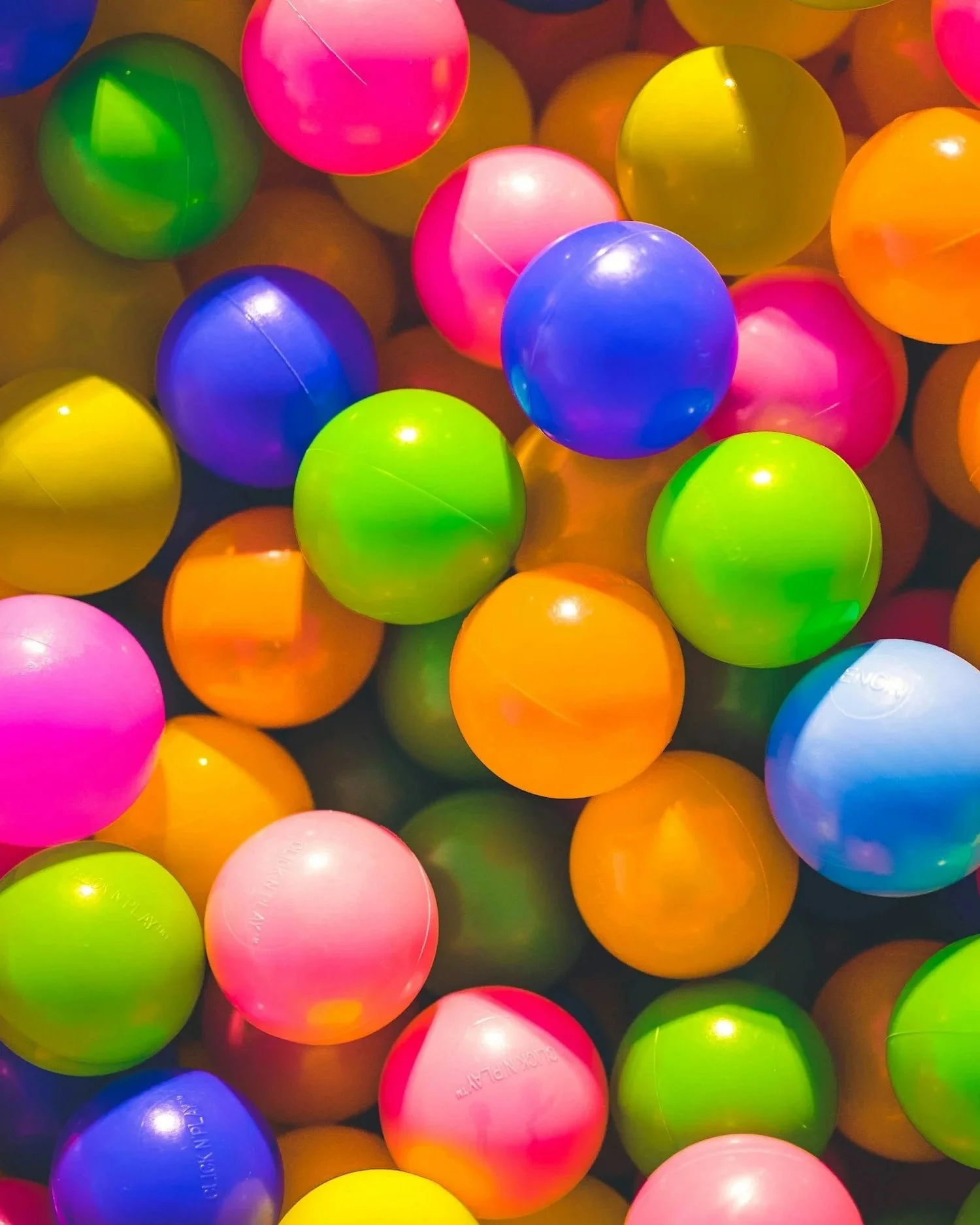 A colorful assortment of plastic playground balls in various bright colors including blue, green, pink, yellow, orange, and purple.