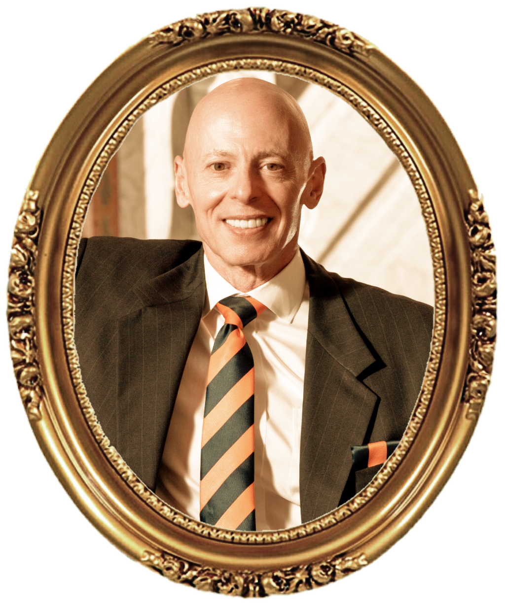 A man with a bald head smiling and wearing a dark suit, white shirt, and a striped tie, looking into a mirror with an ornate gold frame.